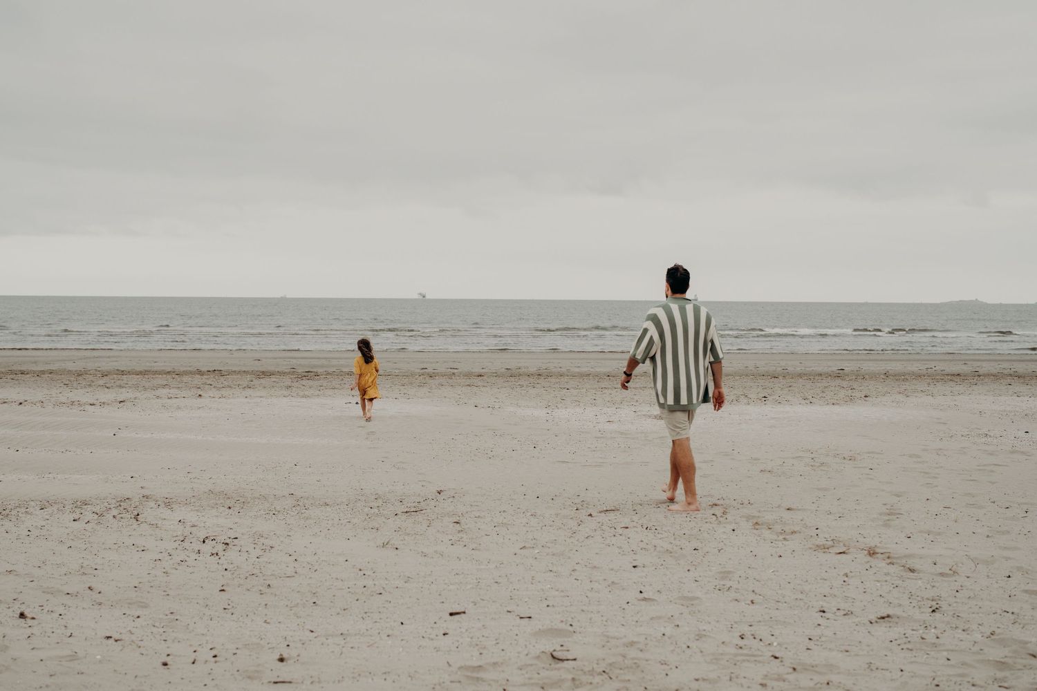 Distant figures walking along a misty beach shoreline on an overcast day.