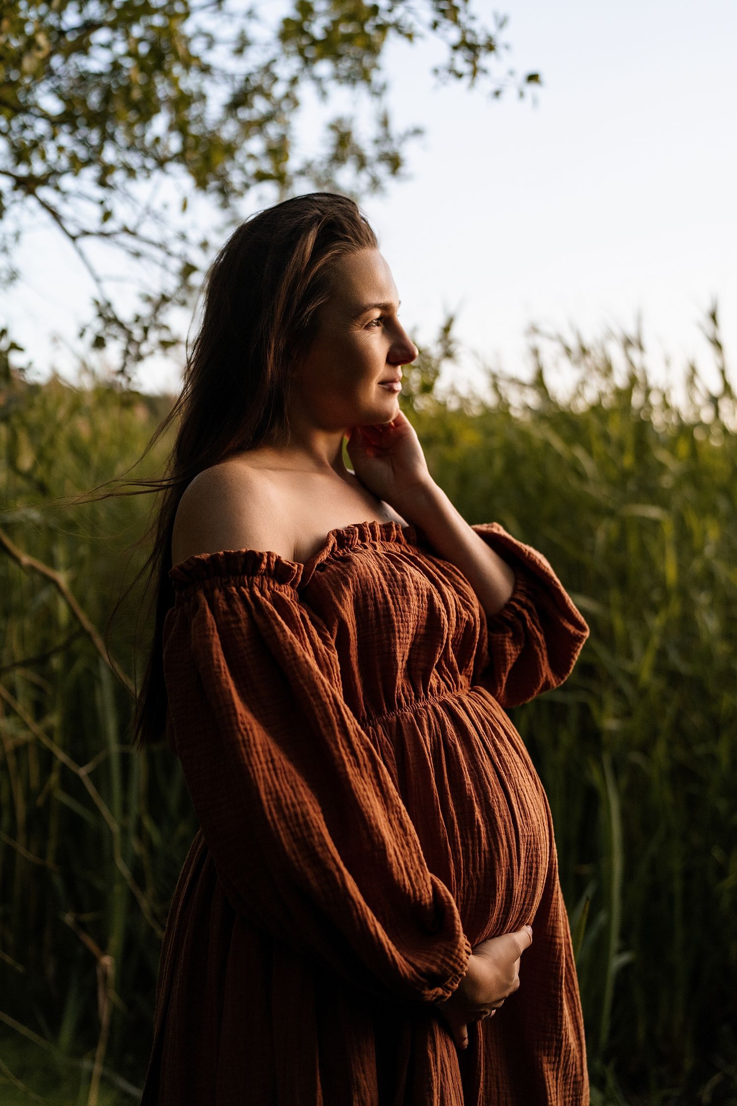 Silhouette maternity portraits in a brown dress against natural foliage.