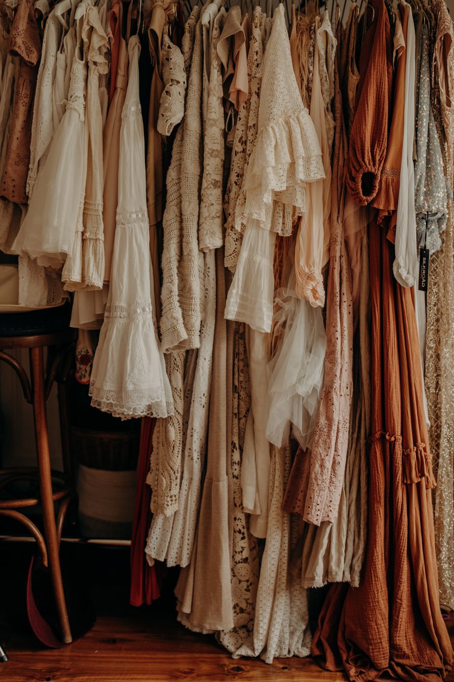 Vintage clothing collection featuring white lace dresses and brown garments hanging on a clothing rack.