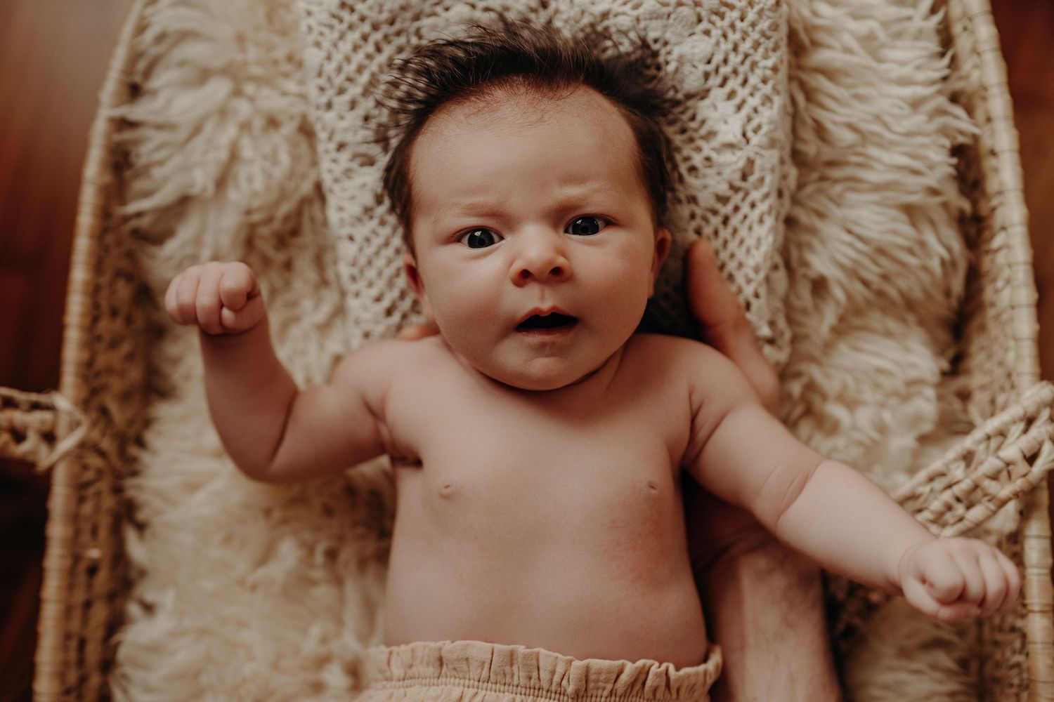Baby resting on textured knit blanket in warm, moody lighting.