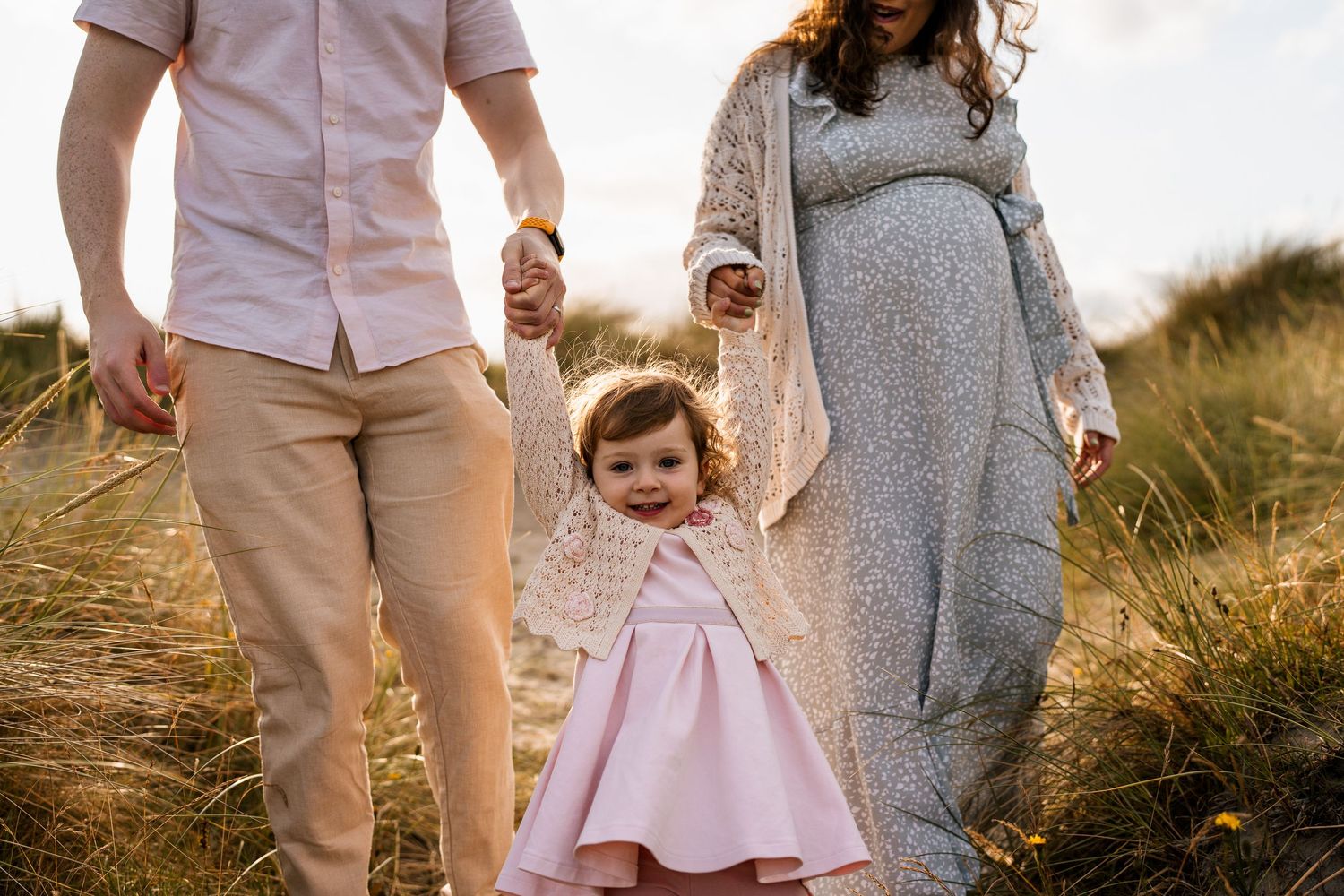 A family walks together through tall grass in a golden field at sunset.