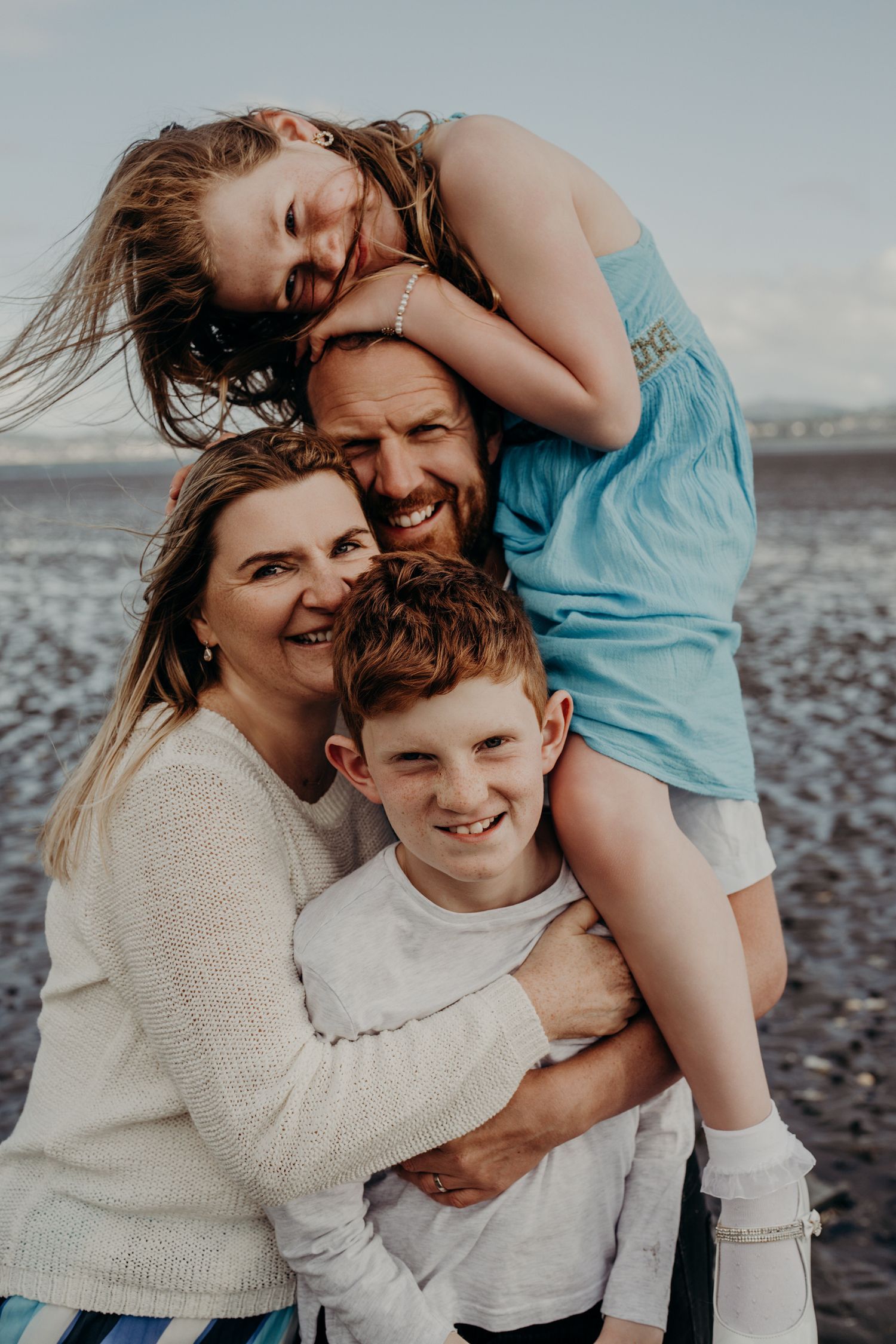 Intimate family portrait showing warm embraces on a rocky beach at sunset.