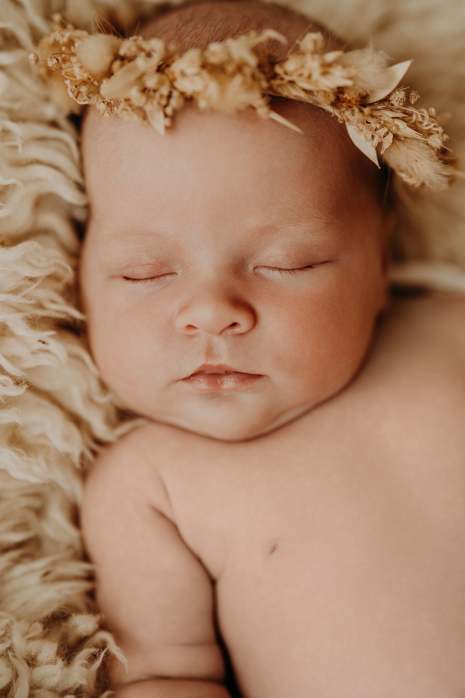 Peaceful sleeping newborn wearing a delicate dried flower crown on soft beige fabric.
