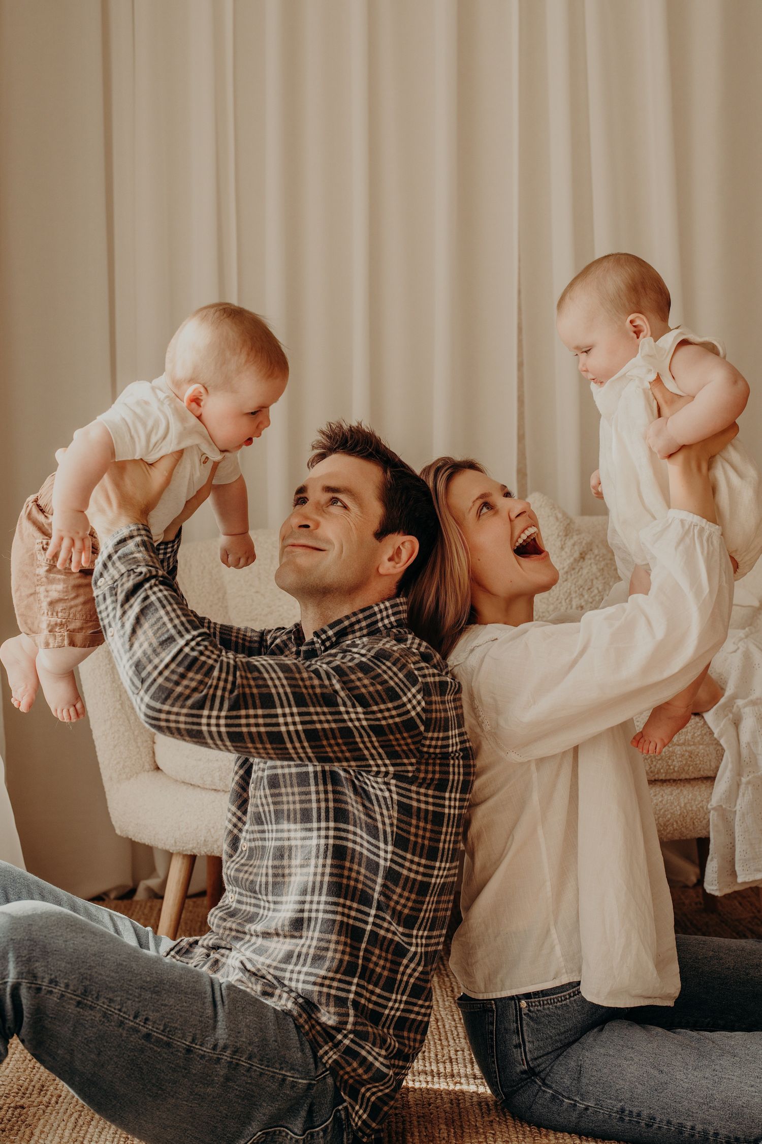 Family plays together on floor with infant in playful poses.