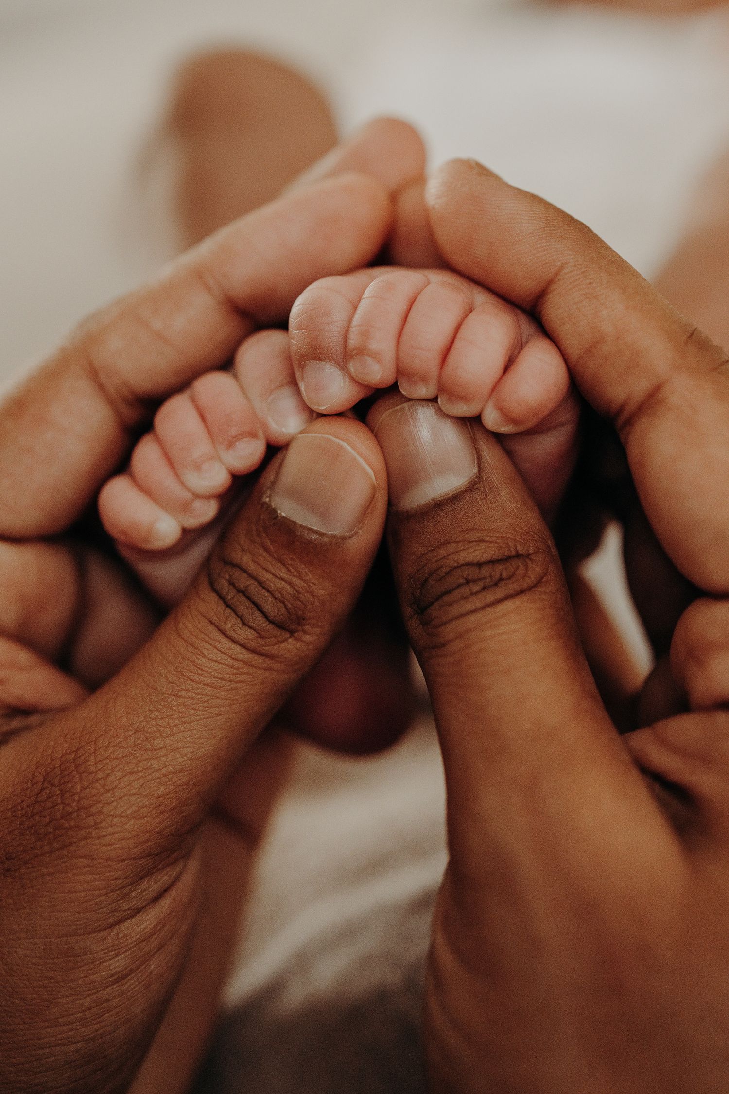 Close-up of gentle hands holding tiny baby toes in warm lighting.