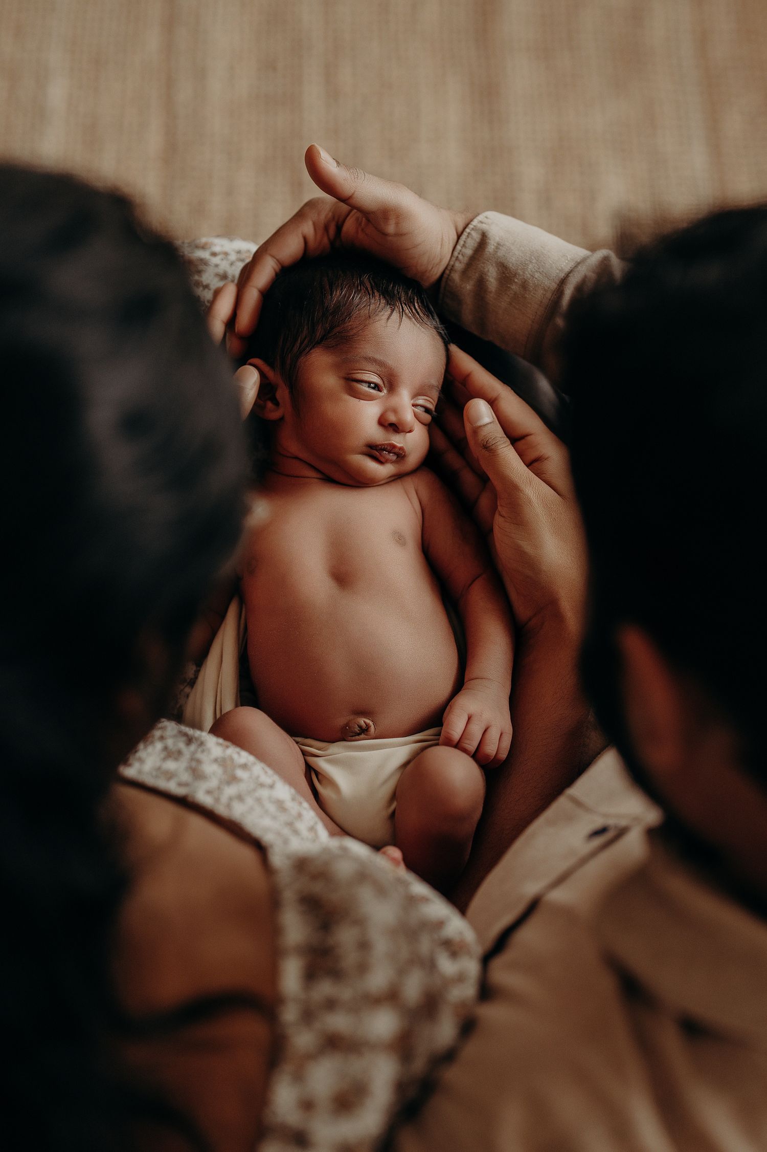 Tender moment with newborn baby being cradled in warm lighting against dark background.