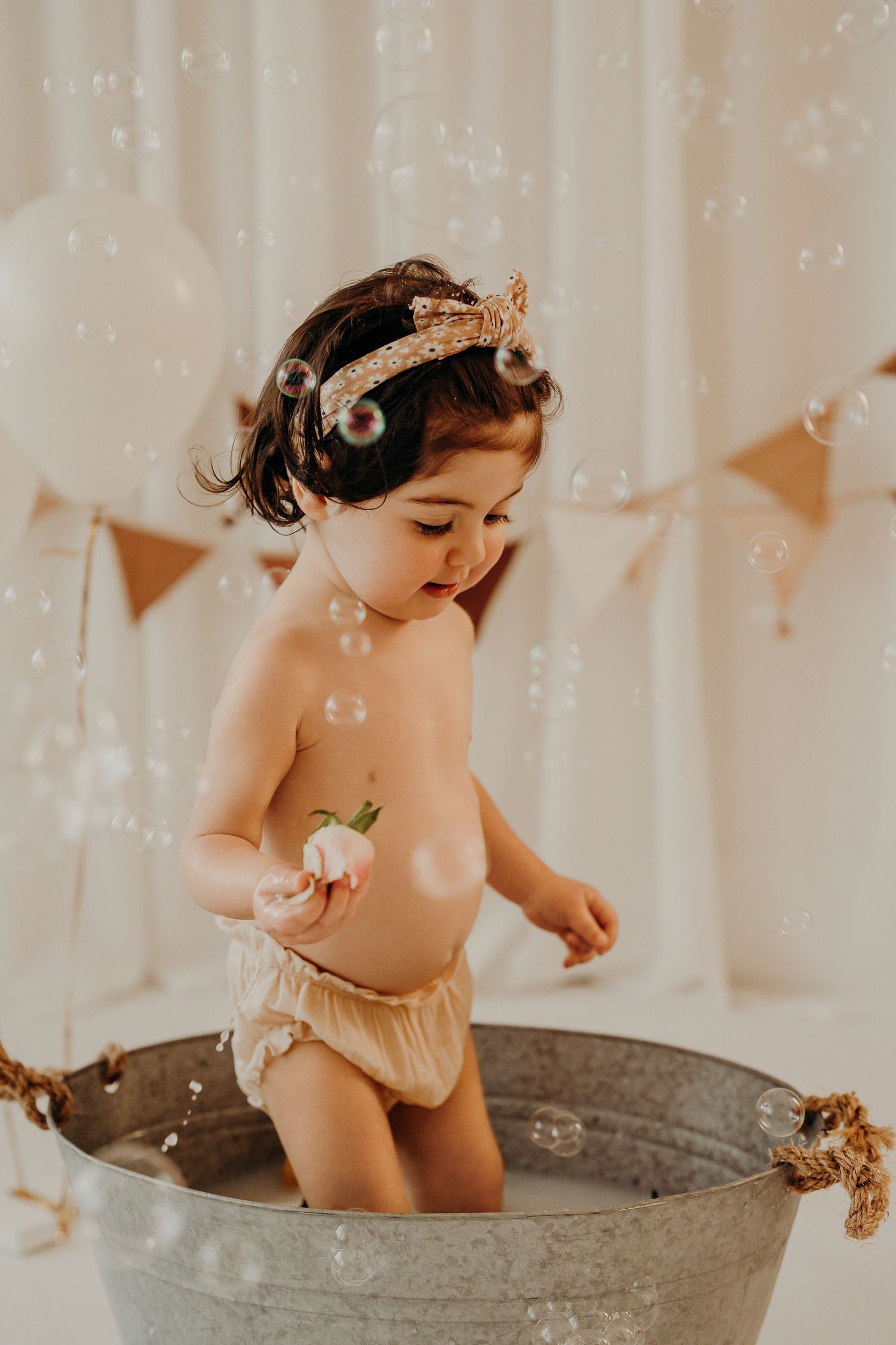 Baby in a vintage metal tub playing with bubbles during a photoshoot with soft lighting.