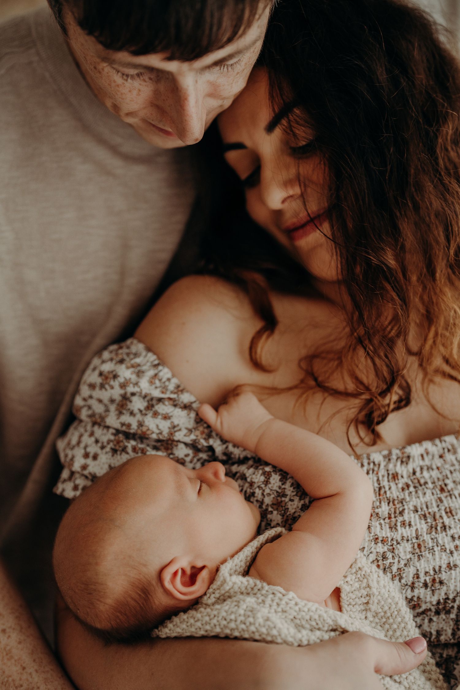 Intimate nursing moment captured in soft natural light with floral dress detail.