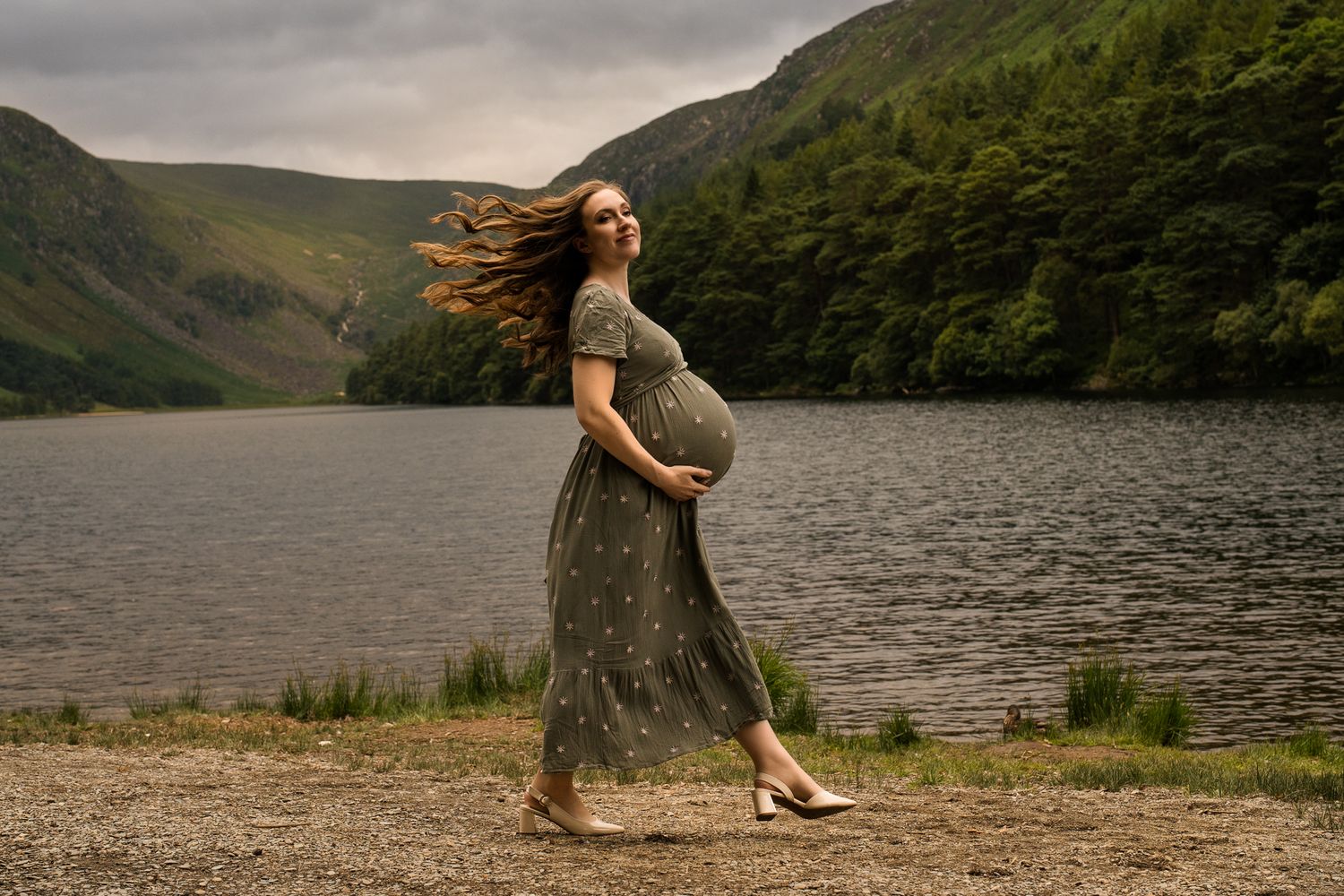 Maternity photo session by scenic lake with mountains in background.