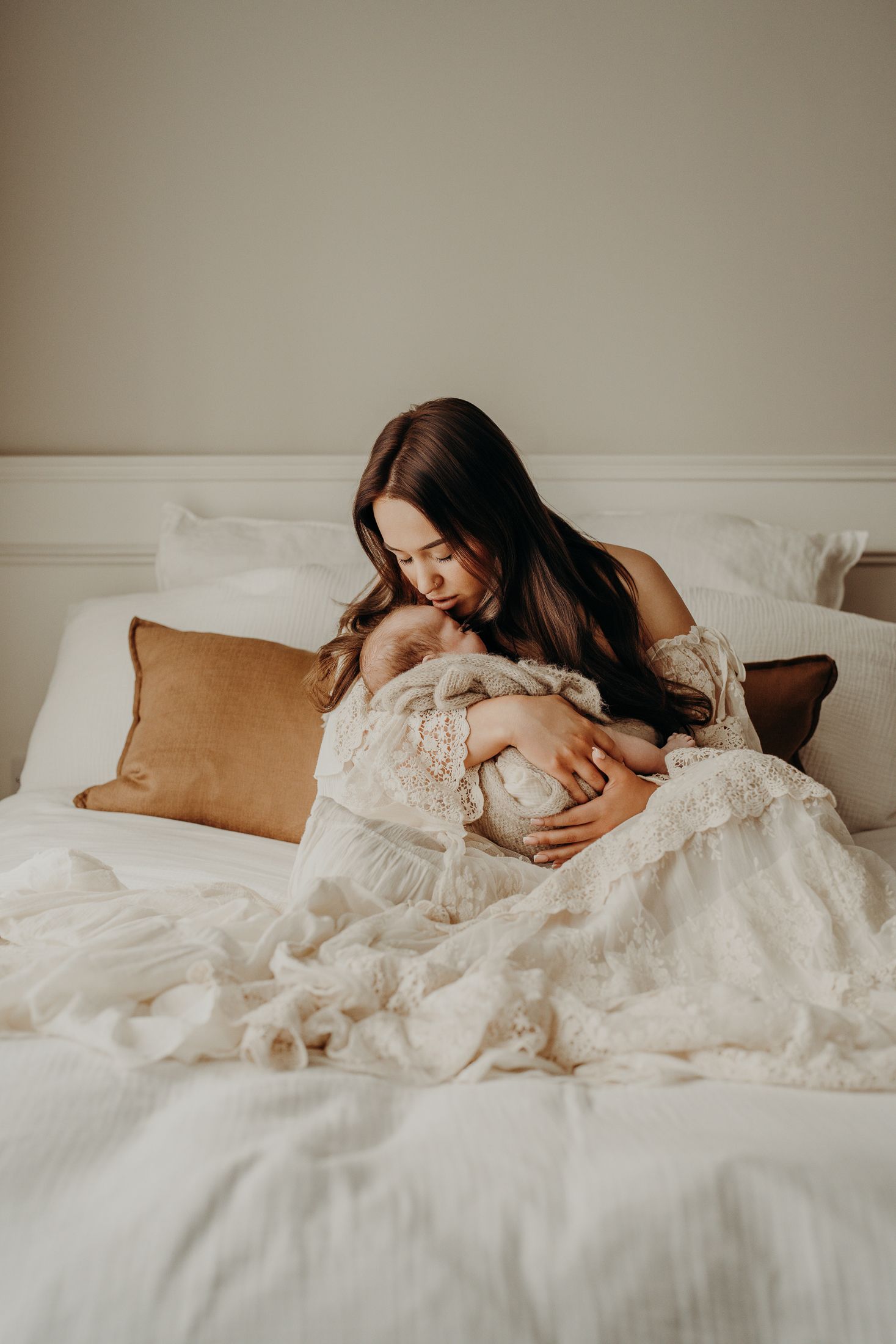 Baby sleeping peacefully in mums arms, white bedding with tan accent pillows in warm natural light. natural newborn sesion dubli