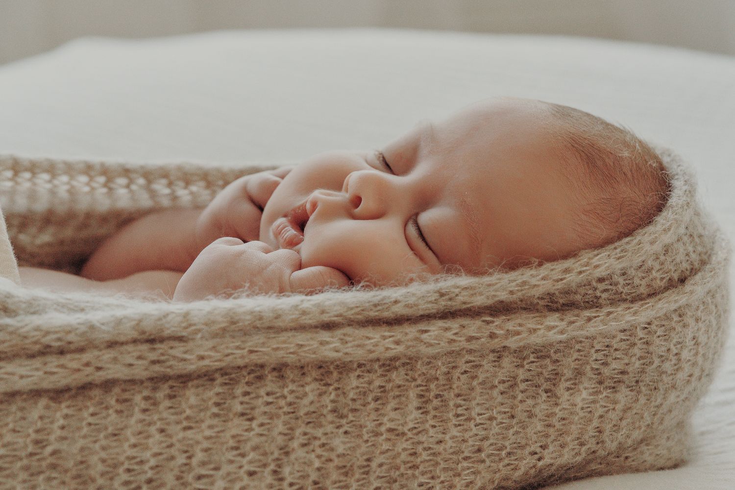 A peaceful sleeping newborn baby wrapped in a cozy beige knitted blanket natural newborn session Dublin.