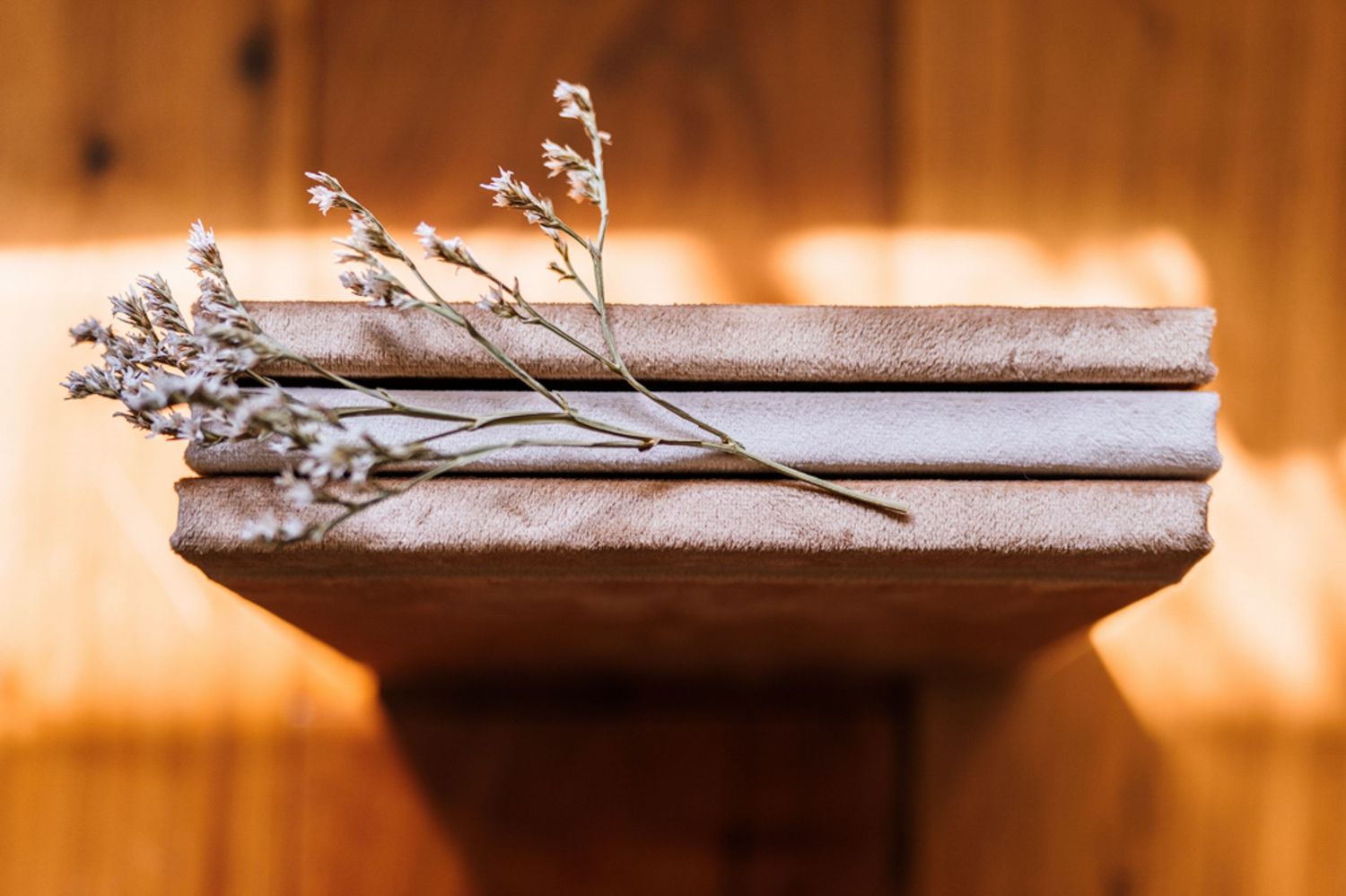 Minimalist photo series showing white books with dried flowers on wooden surface.