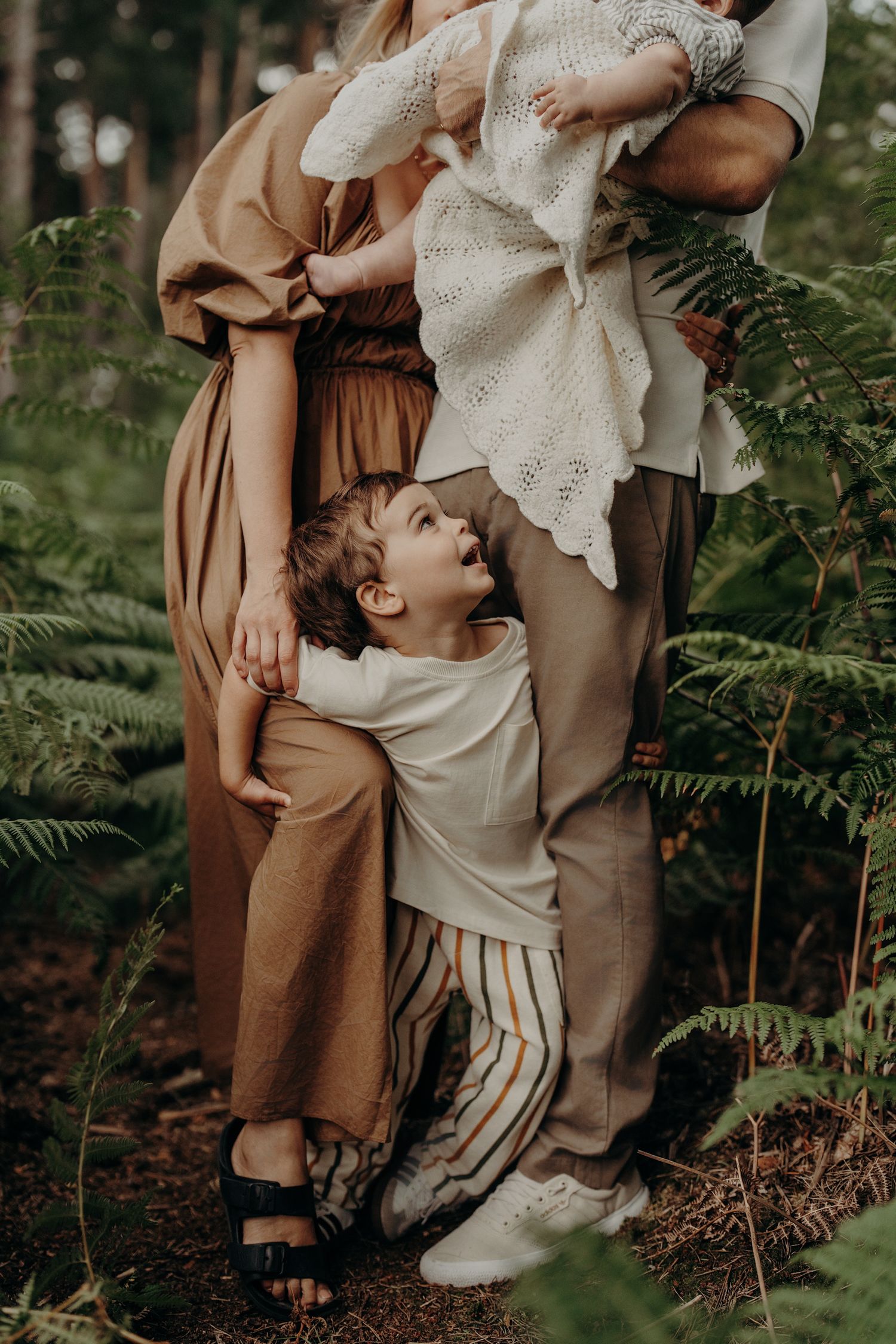 Candid family moment captured in a forest setting with ferns and natural lighting.