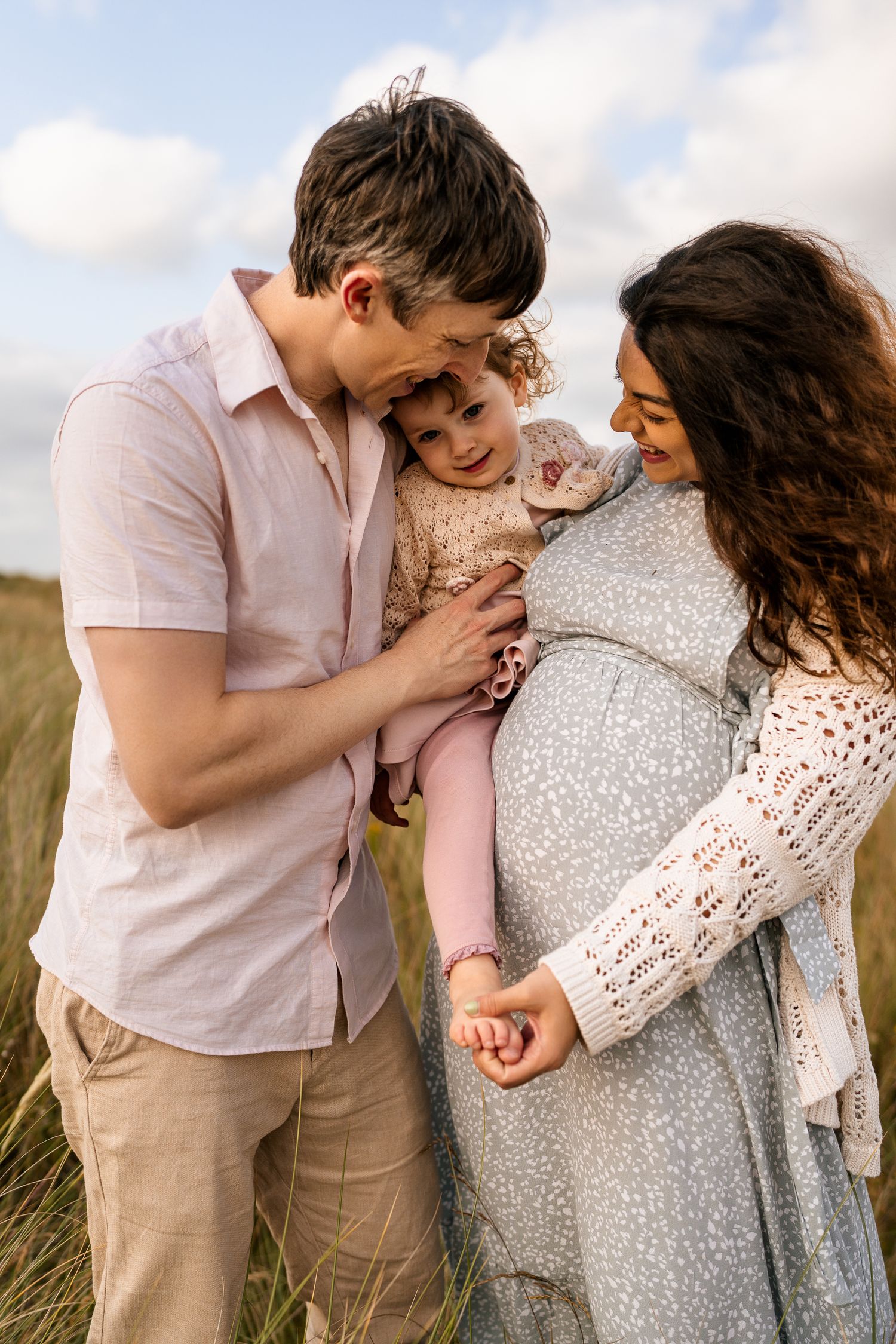 A family shares a tender moment together in a sunlit field of grass.