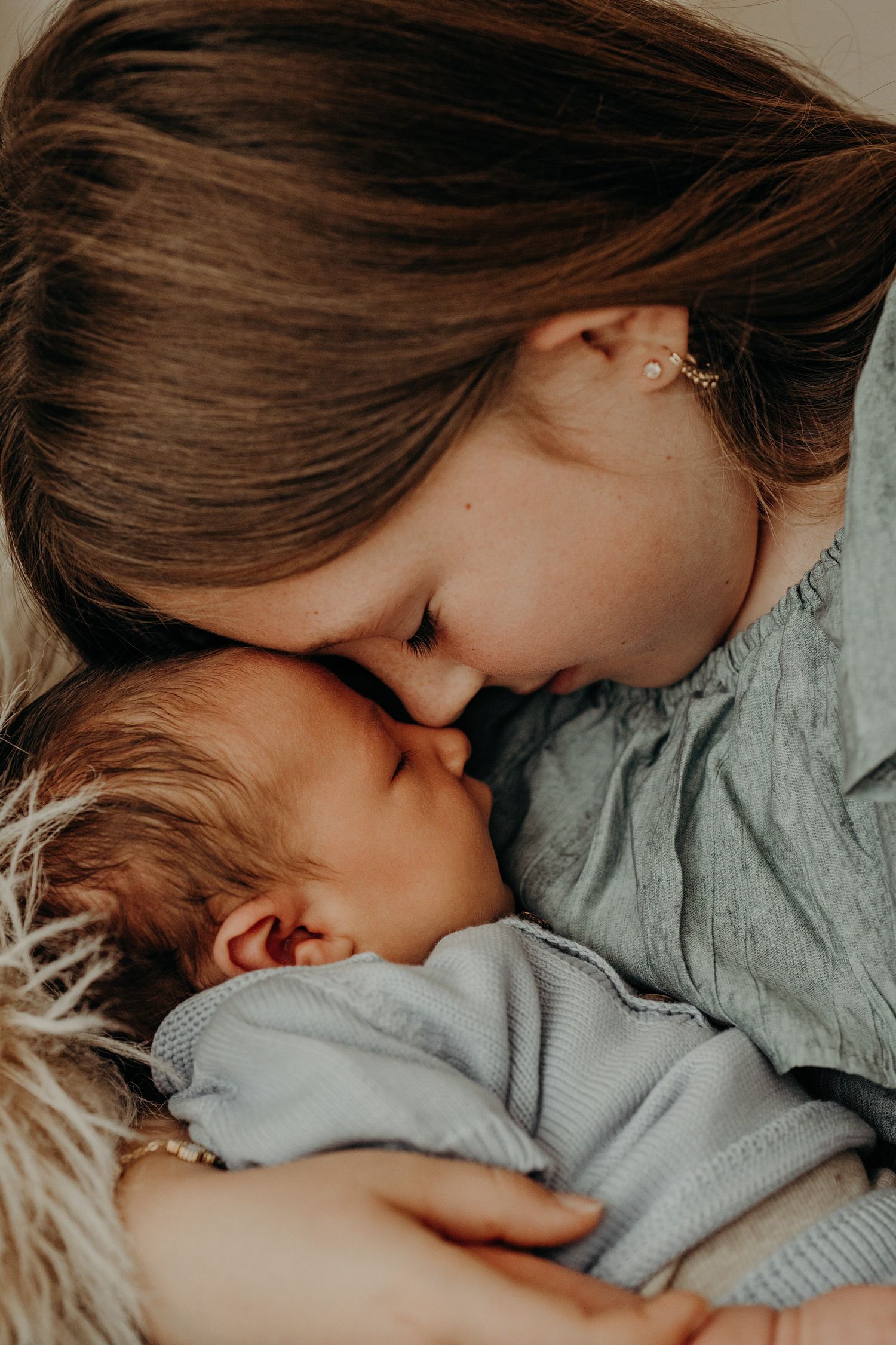 Tender moment between sister and newborn baby in soft lighting showing gentle affection and bonding.