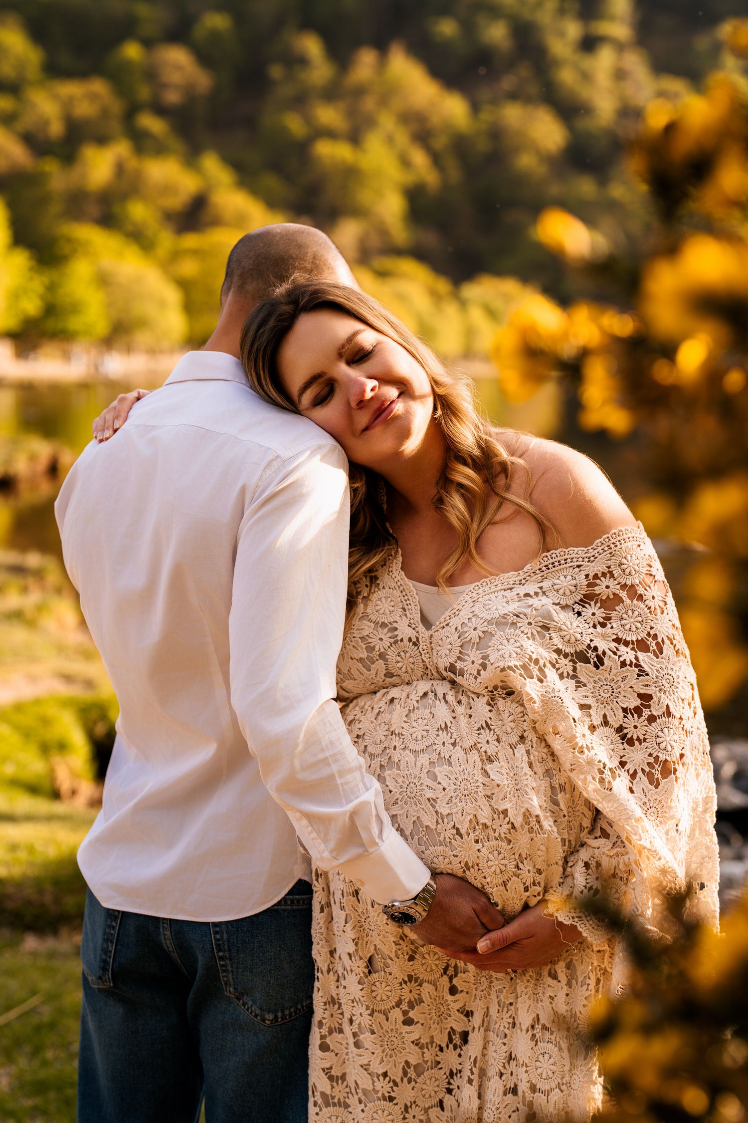 Intimate couple portrait in lace dress against autumn foliage background.