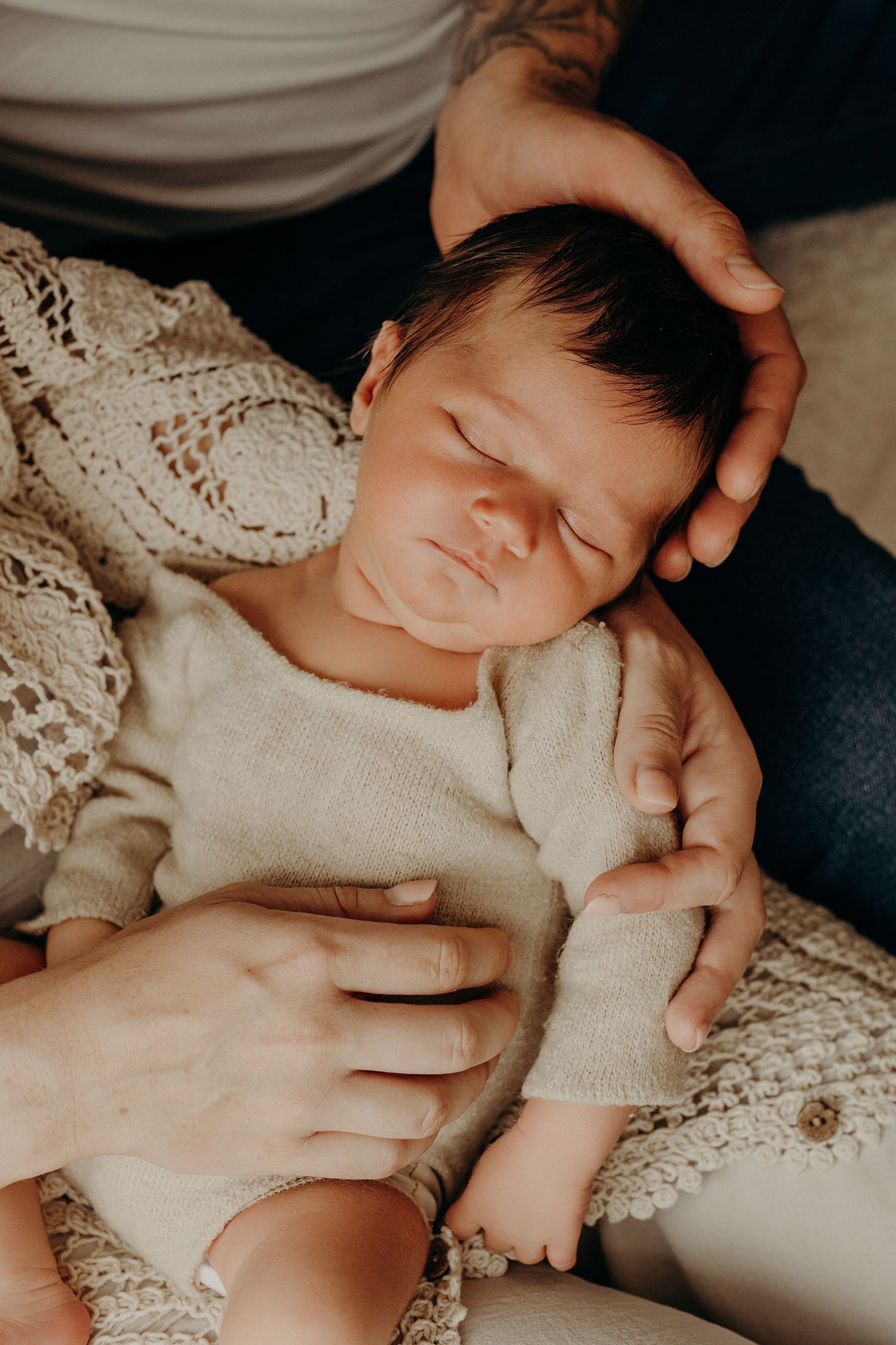 Peaceful newborn baby sleeping in white lace blanket with caring hands nearby.