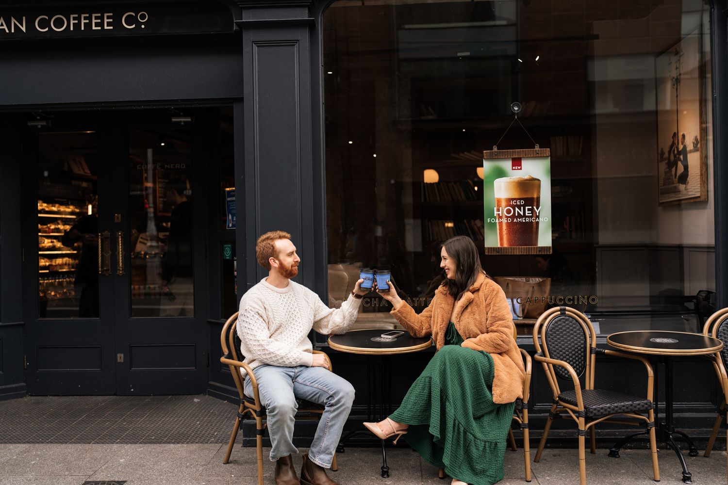 Two people sitting at a cafe table on a city street, enjoying a conversation and drinks.
