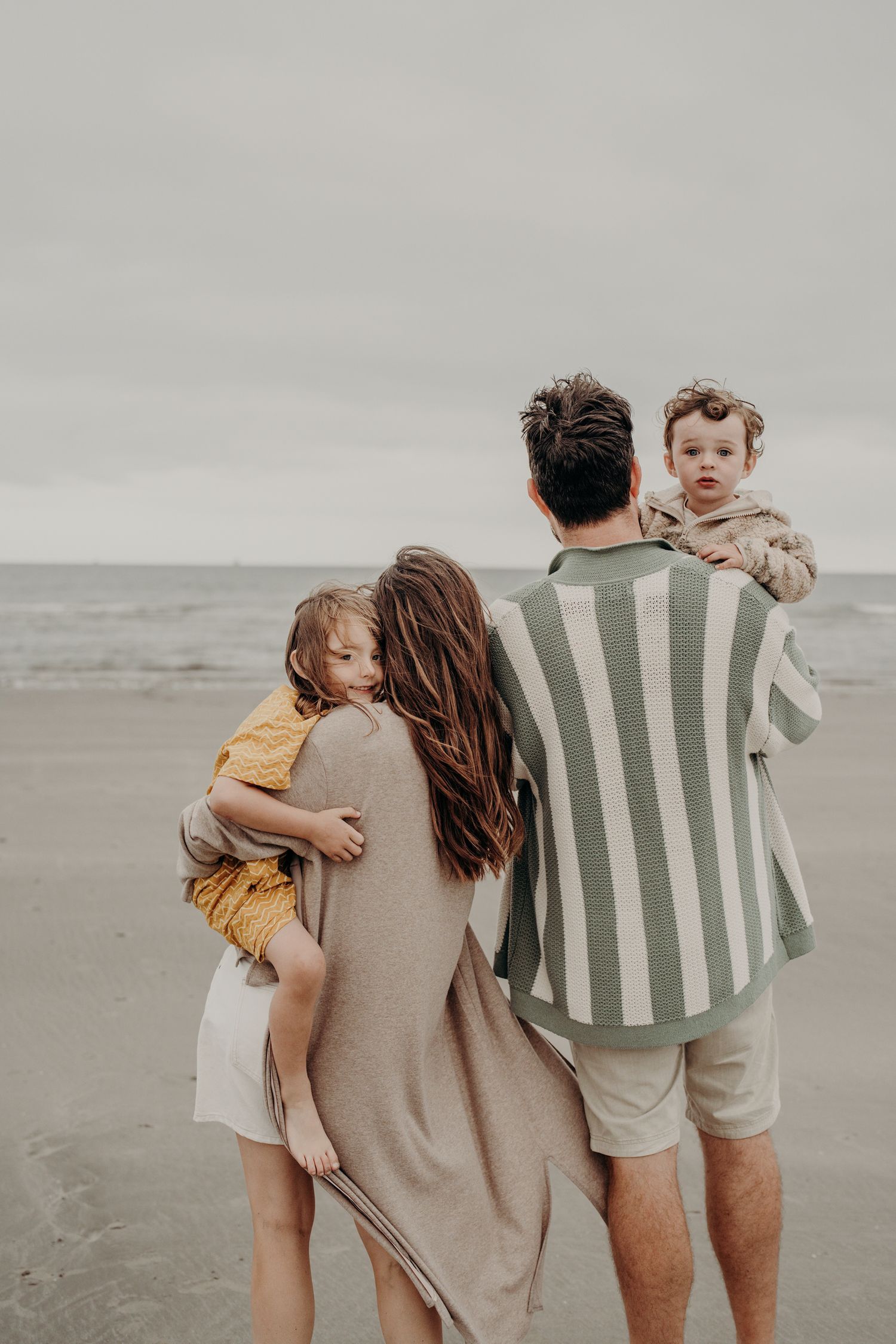 Family embracing while wearing coordinated casual outfits on a moody beach.
