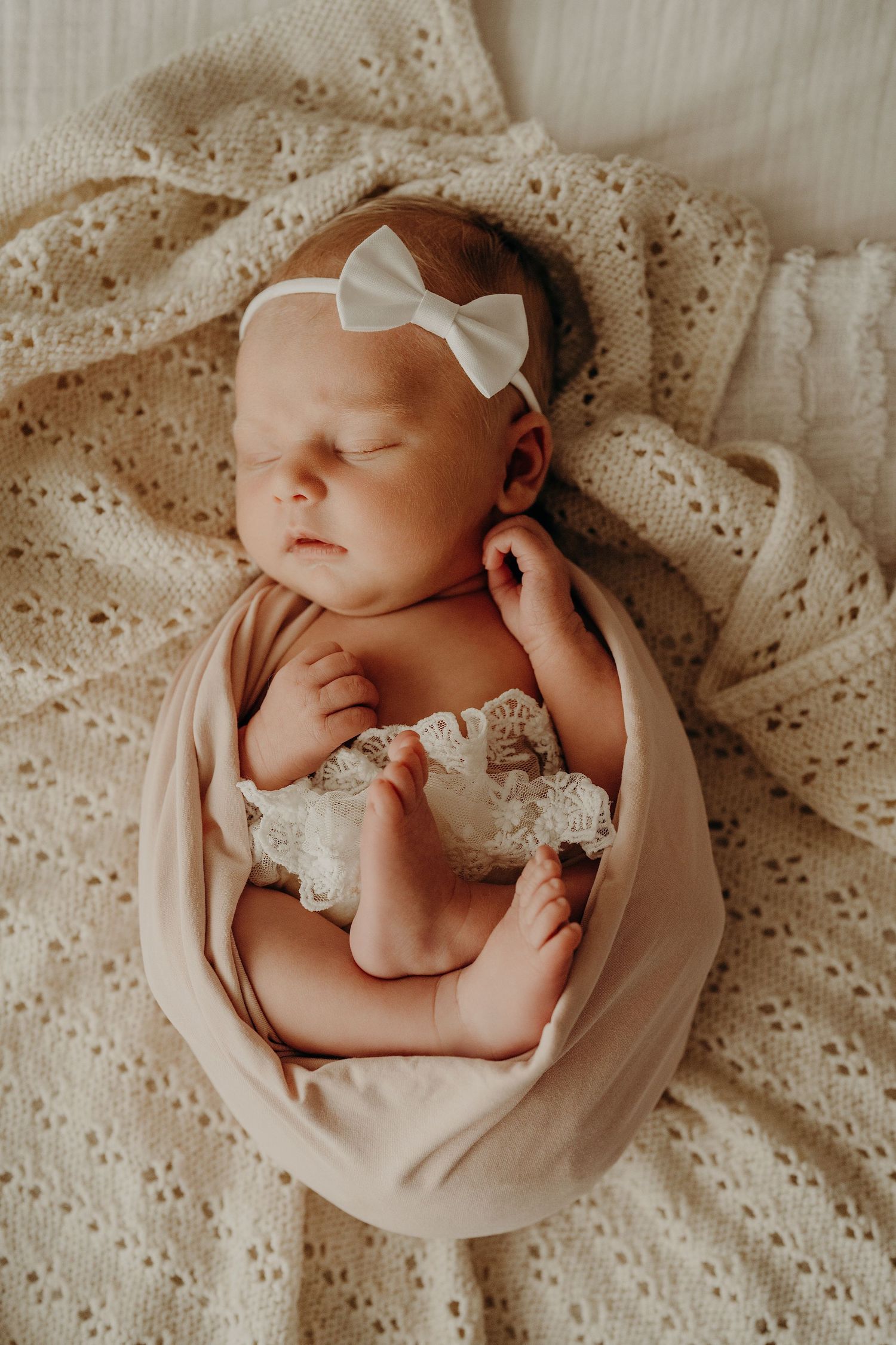 Newborn baby wrapped in cream fabric sleeping peacefully on lace blanket.