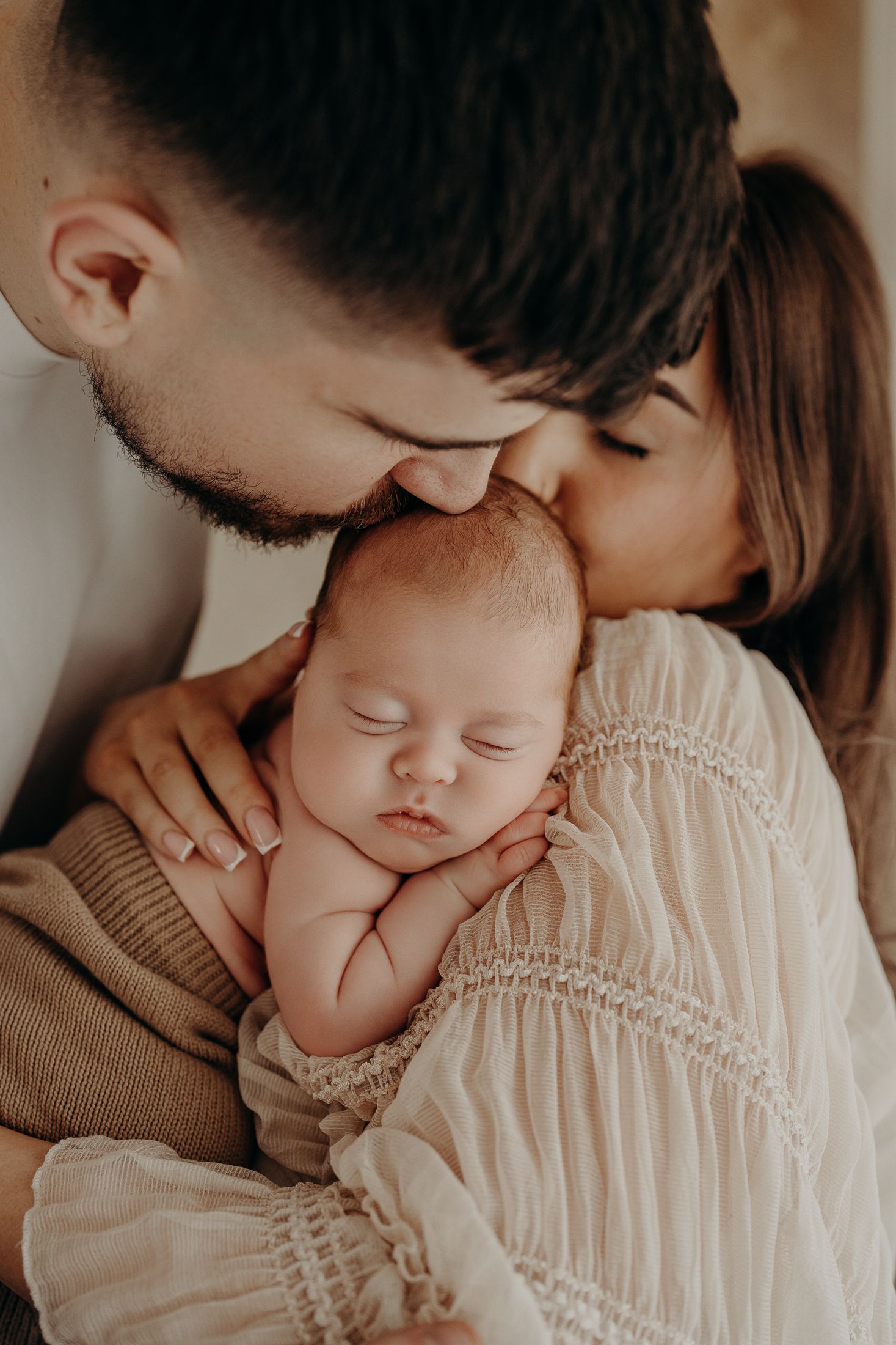 Tender moment between parent and sleeping baby in warm neutral tones captured in a series of intimate photographs, natural newborn session