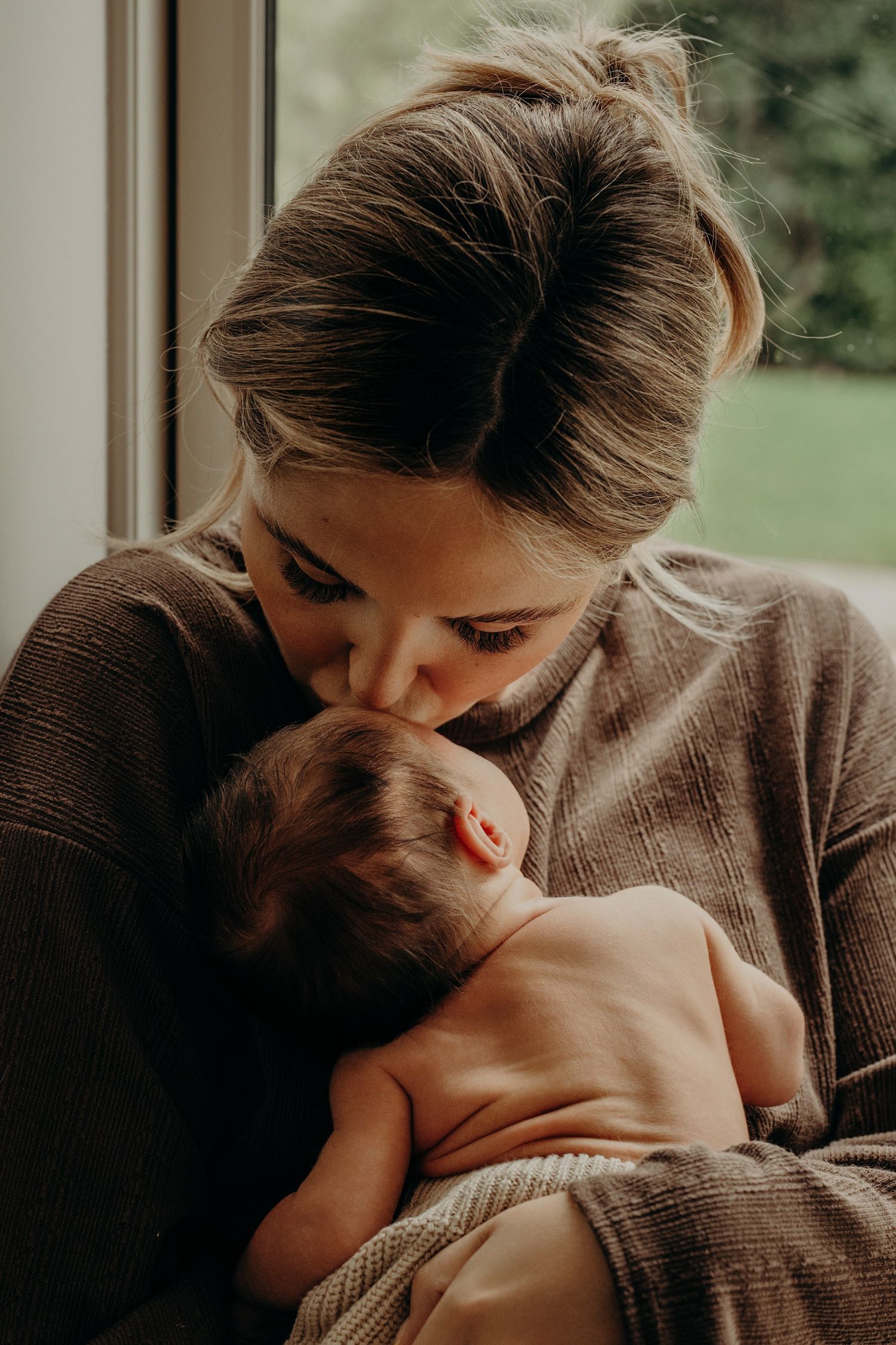 Intimate bonding moment between parent and baby near window in warm brown tones.