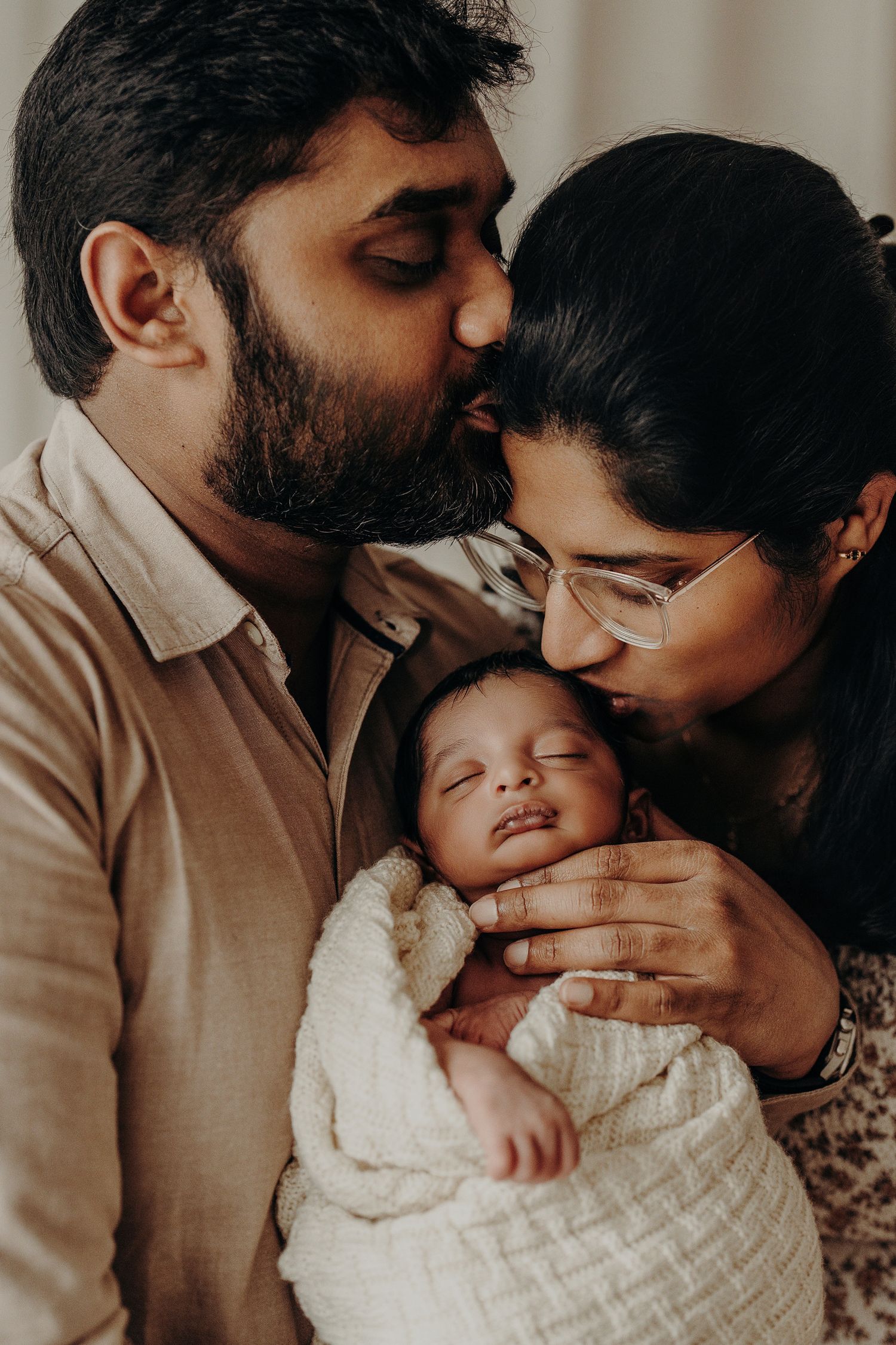 Tender family moment with sleeping newborn wrapped in white blanket.