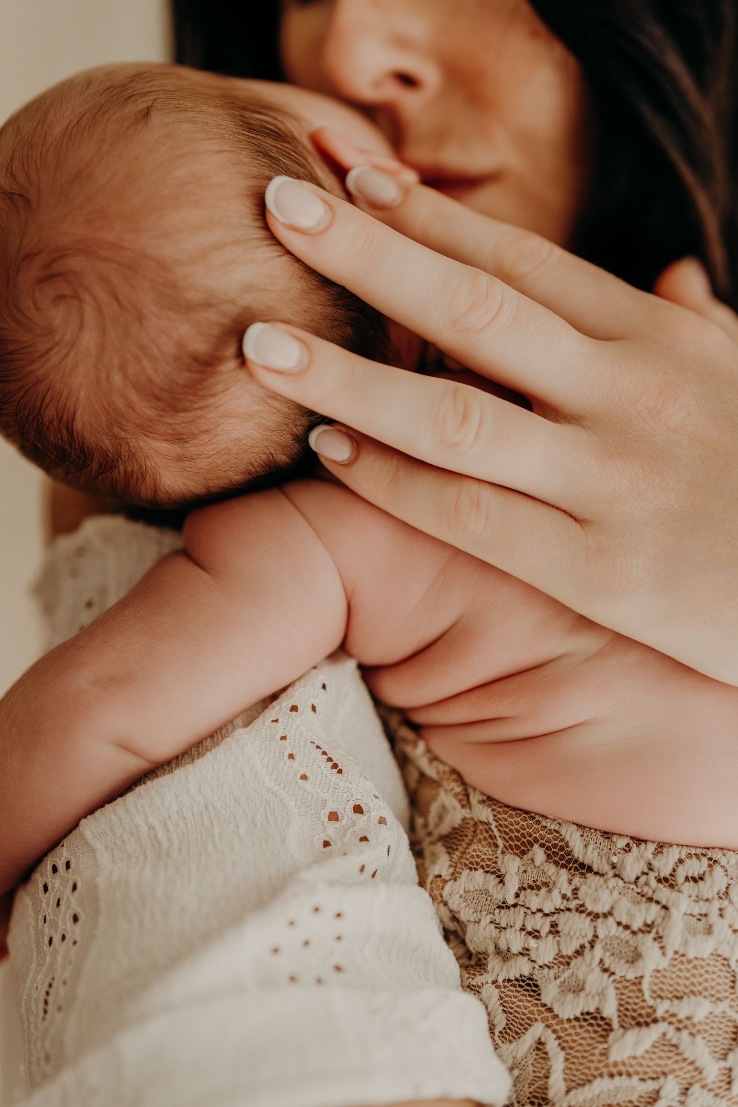 Close-up of gentle hands cradling a newborn baby's head against lace fabric.