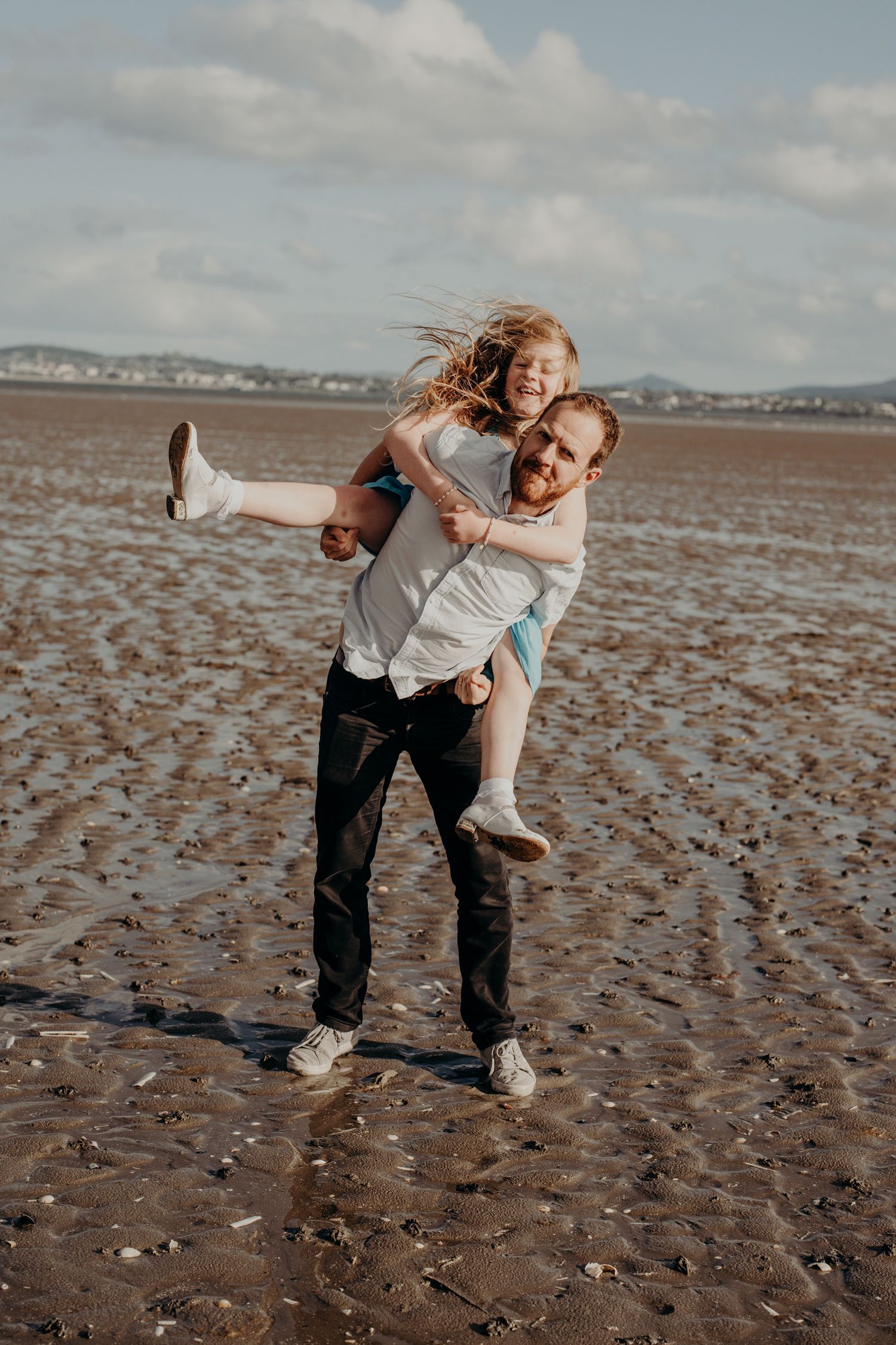 Playful piggyback rides and laughter shared on a textured sandy beach.