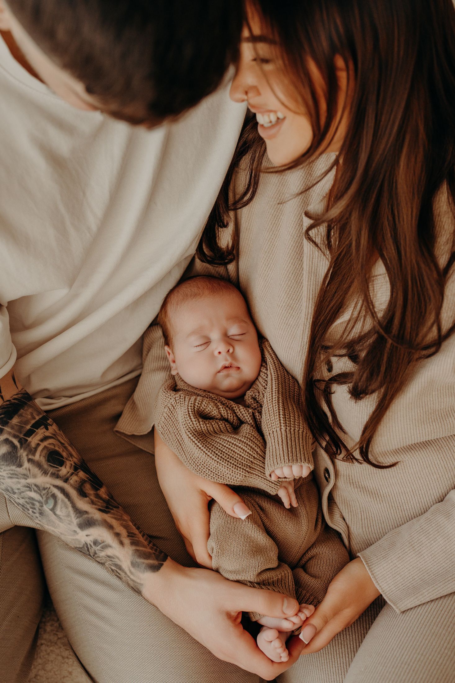 A sleeping newborn baby nestled between parents wearing neutral tones in an intimate studio newborn session.