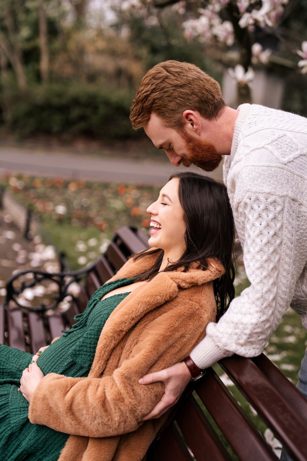 A happy couple shares a tender moment on a park bench surrounded by spring blossoms.