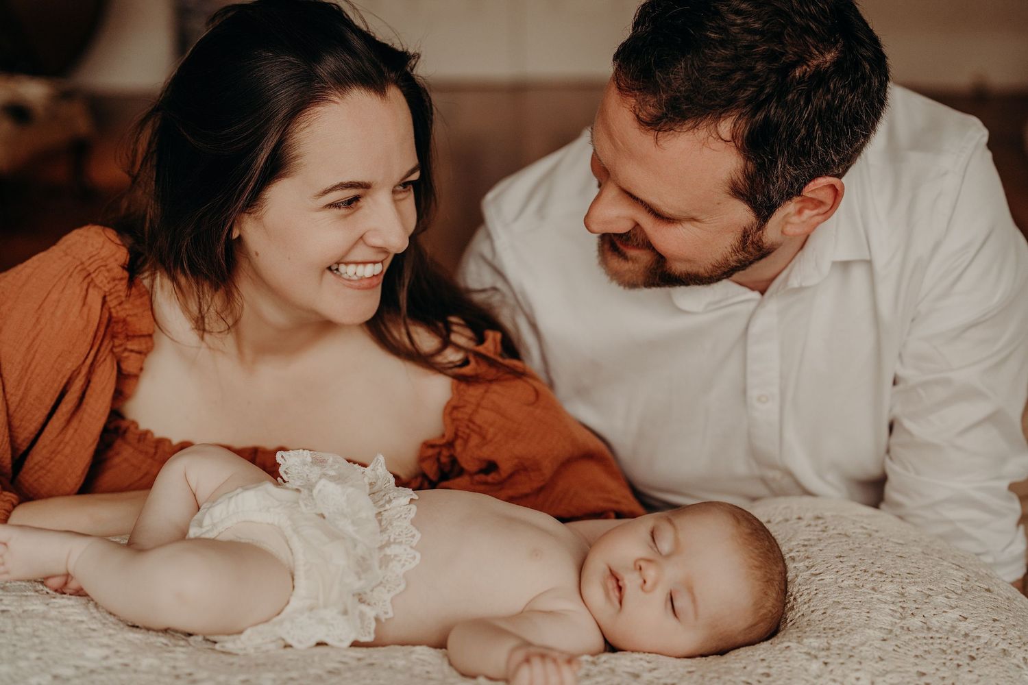 Intimate family lifestyle session captured on cream colored bedding in warm lighting.
