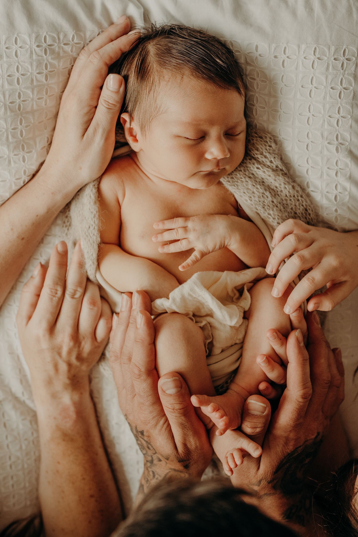 Gentle hands tenderly holding sleeping newborn on textured white surface.