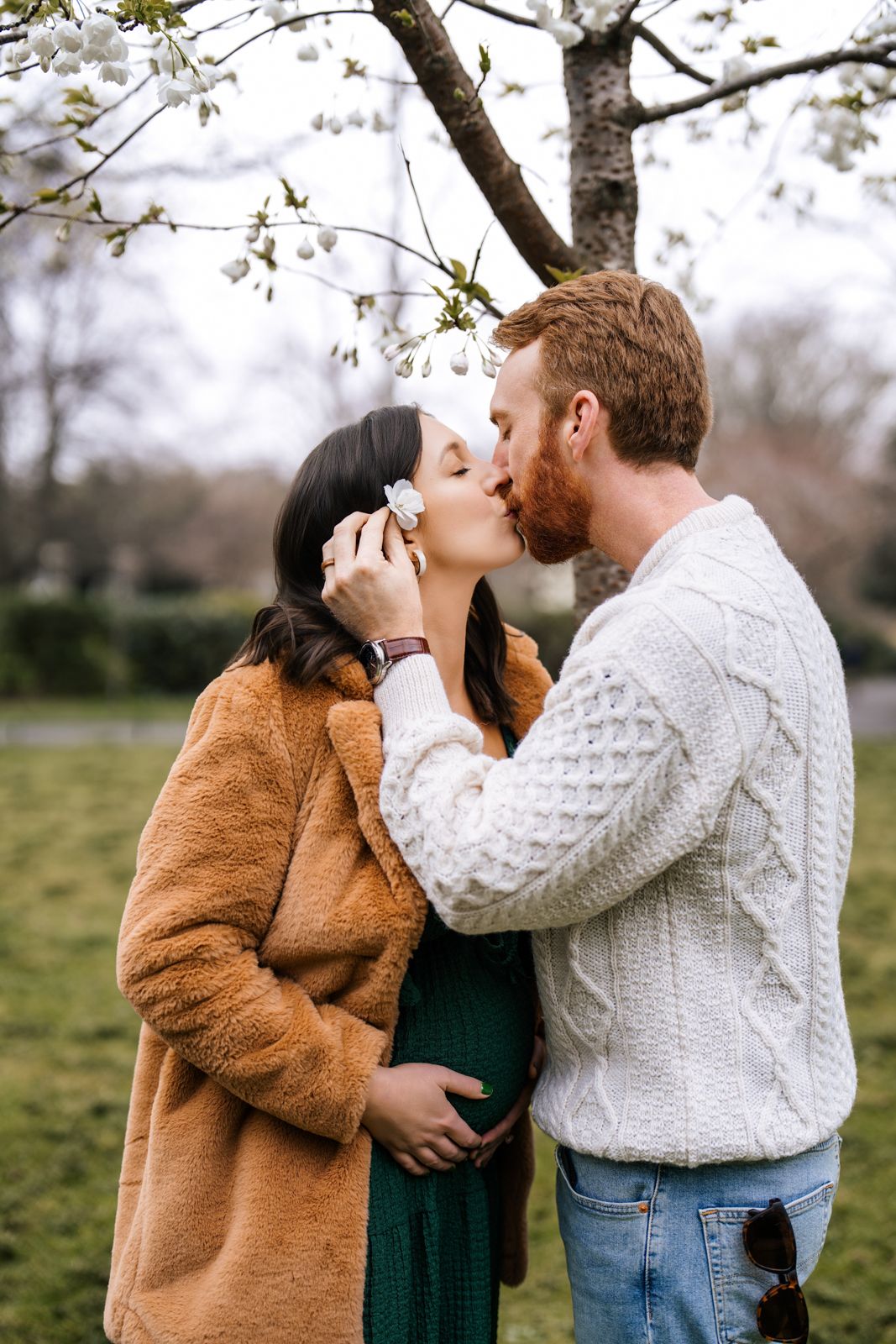 A couple embracing and kissing in a snowy outdoor setting with a blurred background of trees.