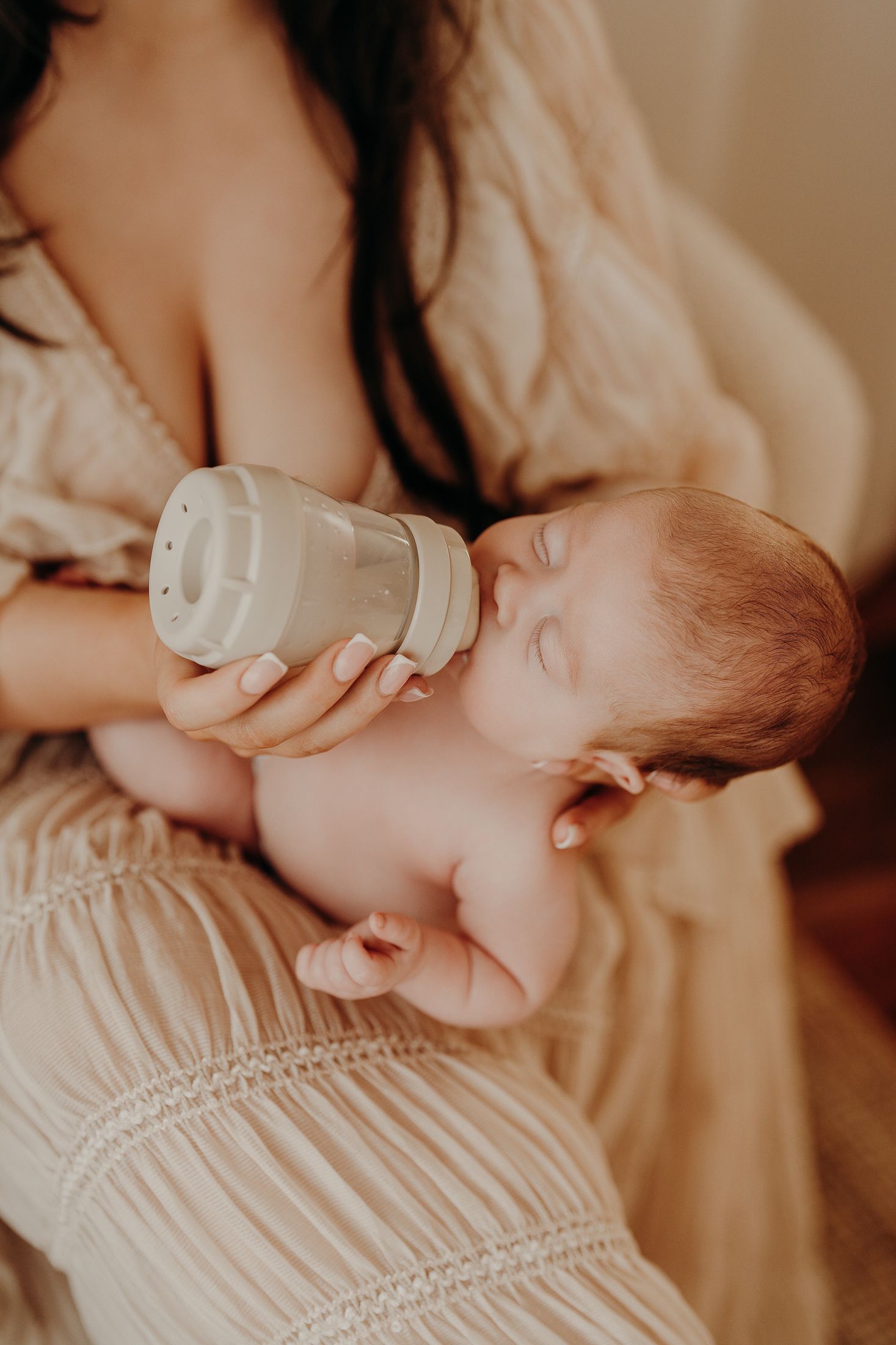 Baby drinks from a bottle while being cradled in soft beige clothing, captured in warm natural lighting. Relaxed newborn session dublin