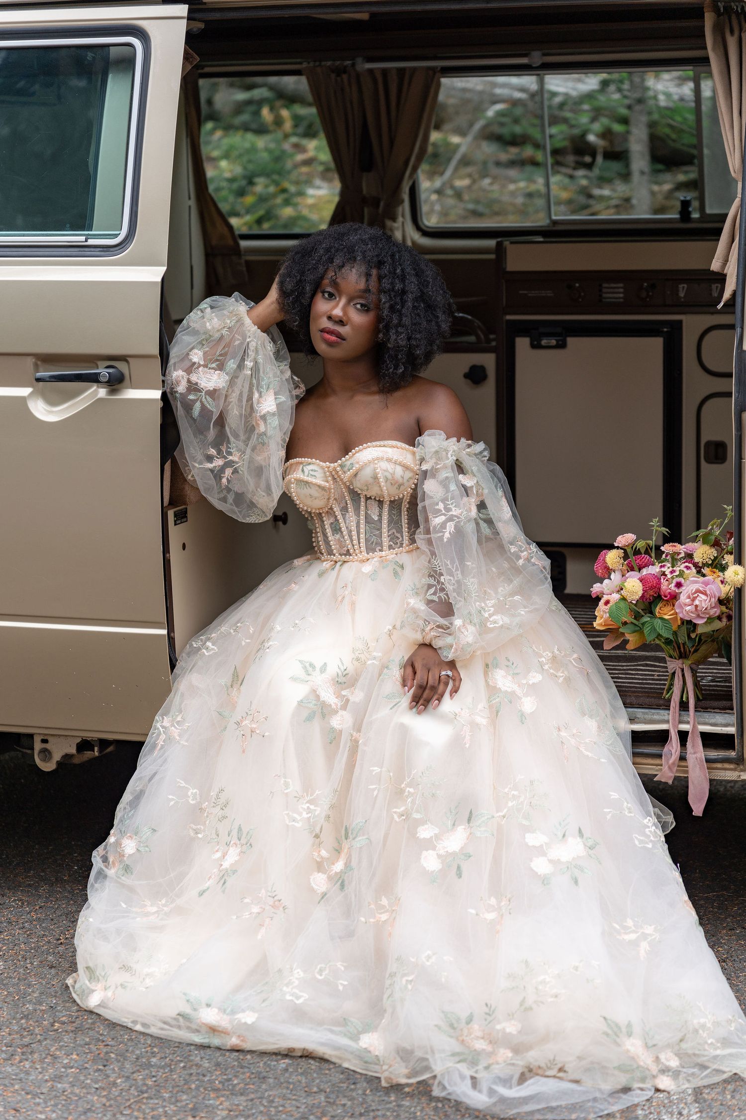 An elegant bridal portrait featuring a flowing white gown with intricate lace details beside a vintage vehicle.