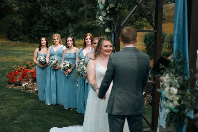 Wedding party members in blue dresses gather outdoors during the ceremony.