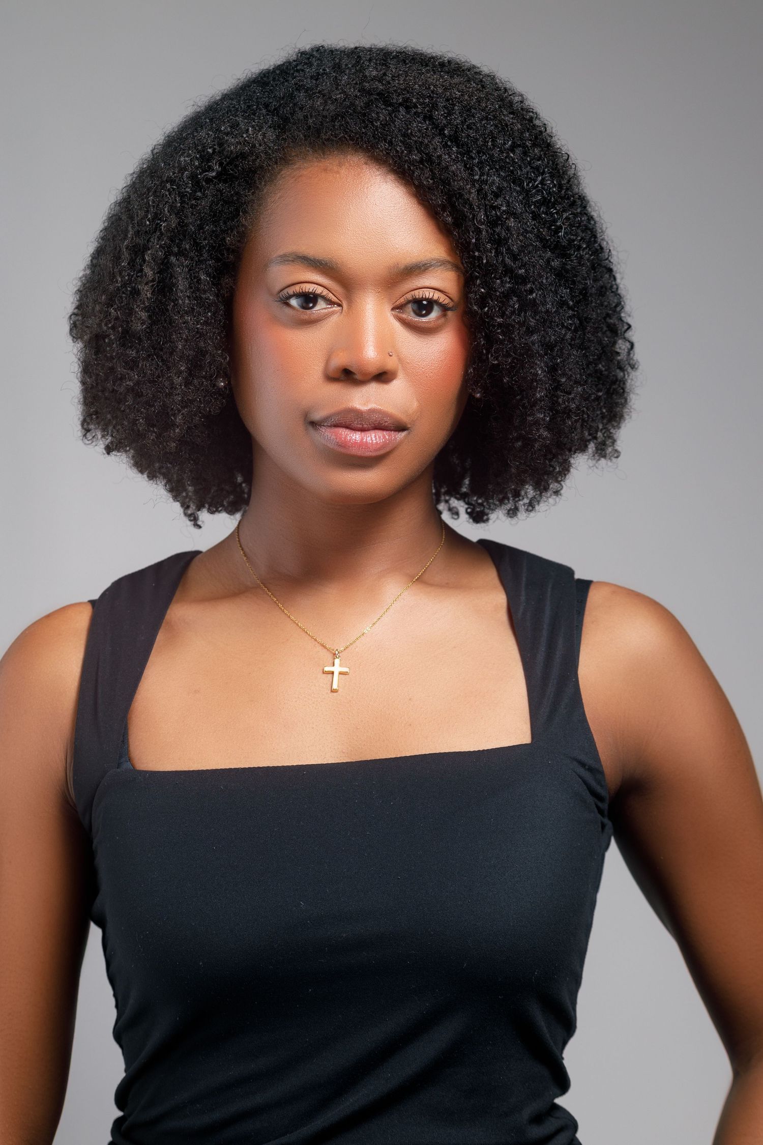 Professional headshots with natural curly hair wearing black sleeveless top and cross necklace.