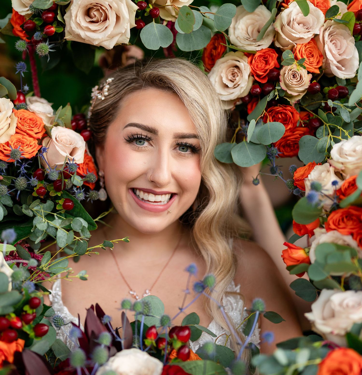 Bridal portrait surrounded by coral roses and eucalyptus floral arrangements.