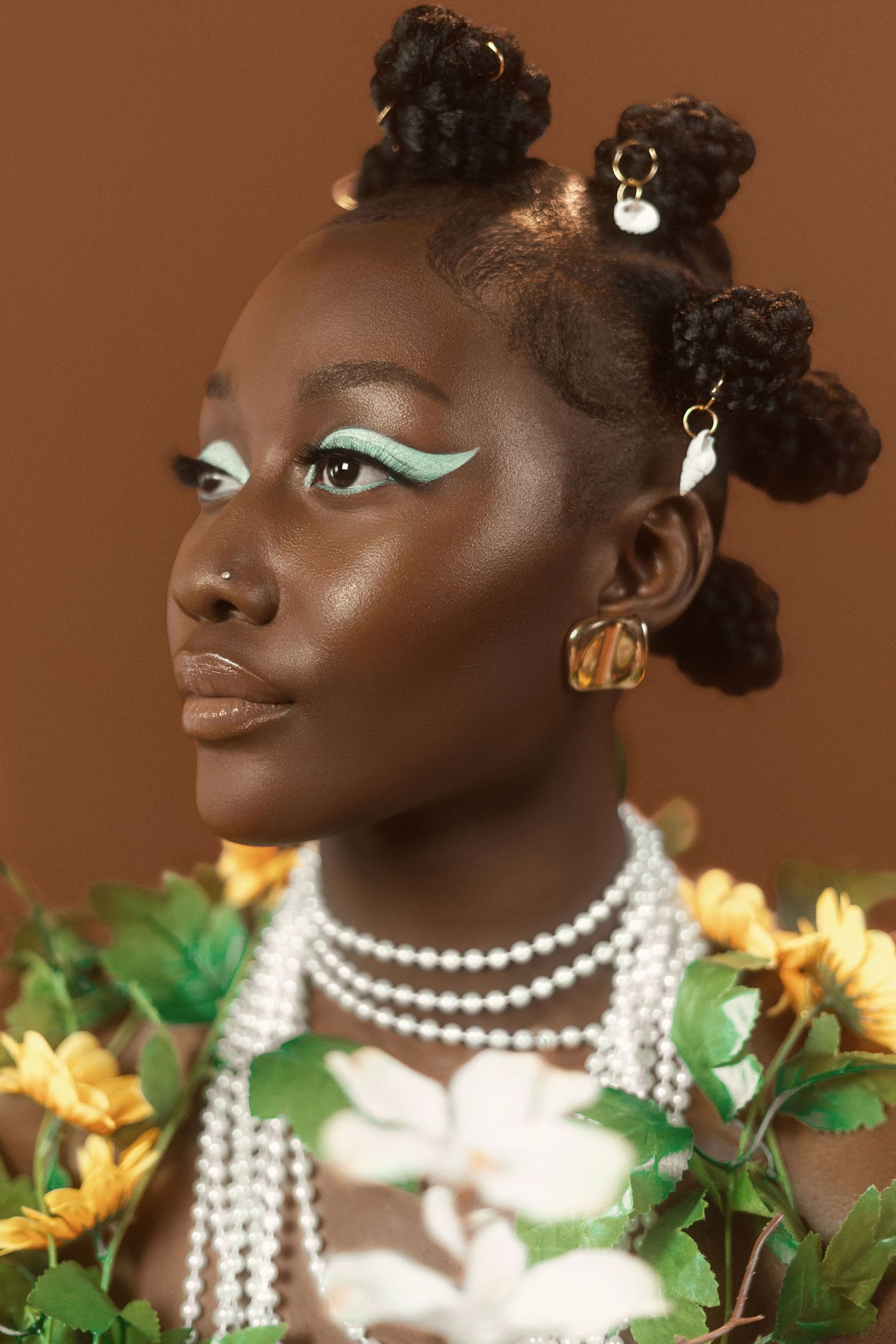 Artistic portrait with pearl necklaces and floral accessories against warm brown backdrop.