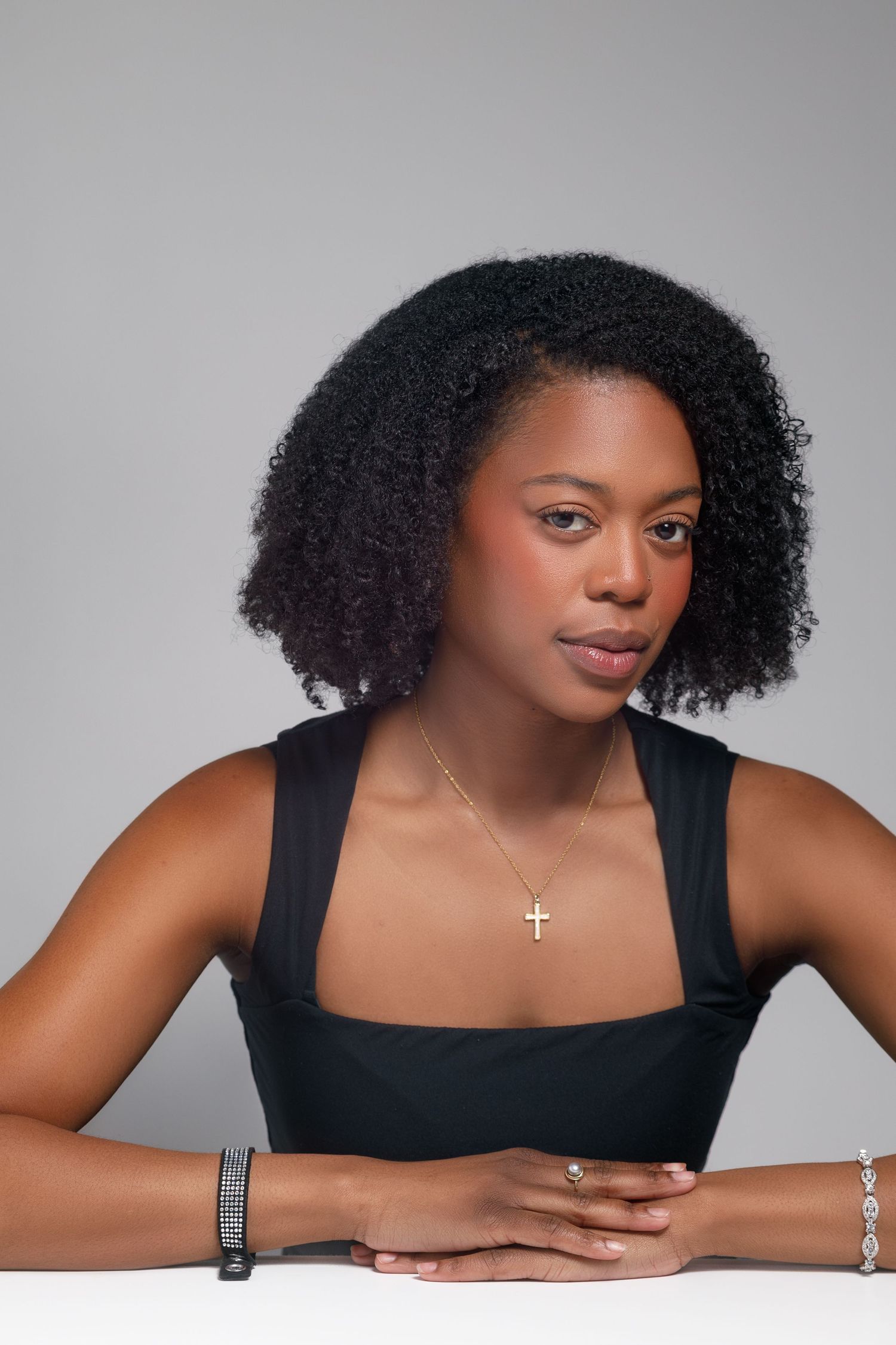 Elegant studio poses in black sleeveless top with natural curly hair and minimal jewelry.