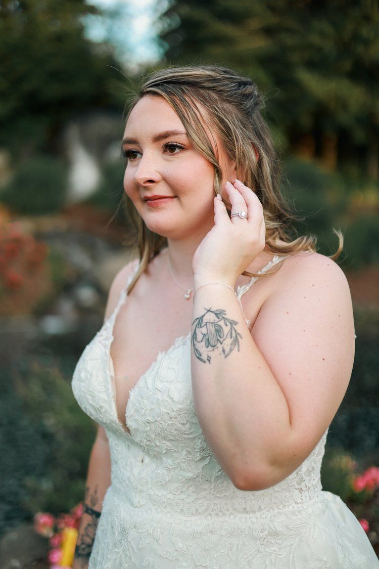 A bride wearing a delicate lace gown poses gracefully against a natural backdrop.