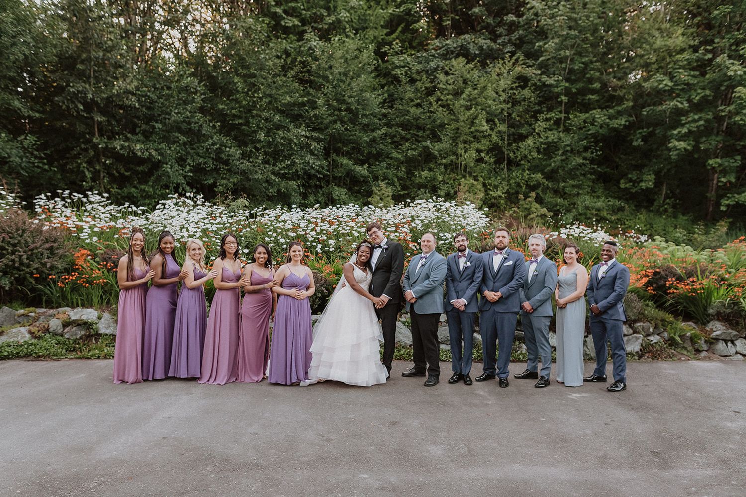 Wide shot of wedding party lined up outdoors wearing purple and gray attire.