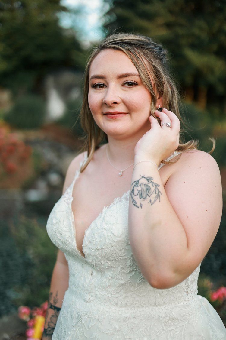 A bride in a lace wedding dress poses elegantly in an outdoor garden setting.