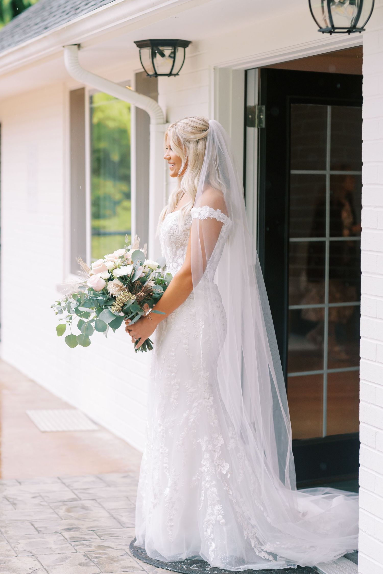 Bride in classic white gown poses along covered walkway with elegant floral bouquet.