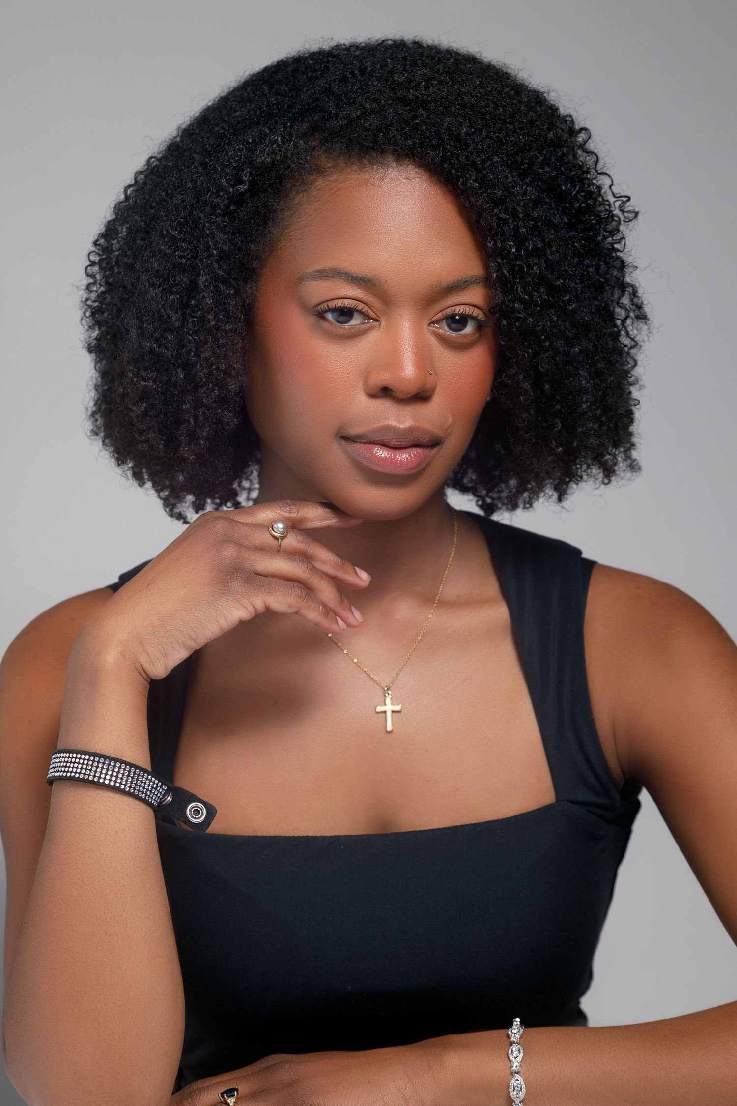 Artistic portrait series showing natural hair and black top with delicate cross necklace.