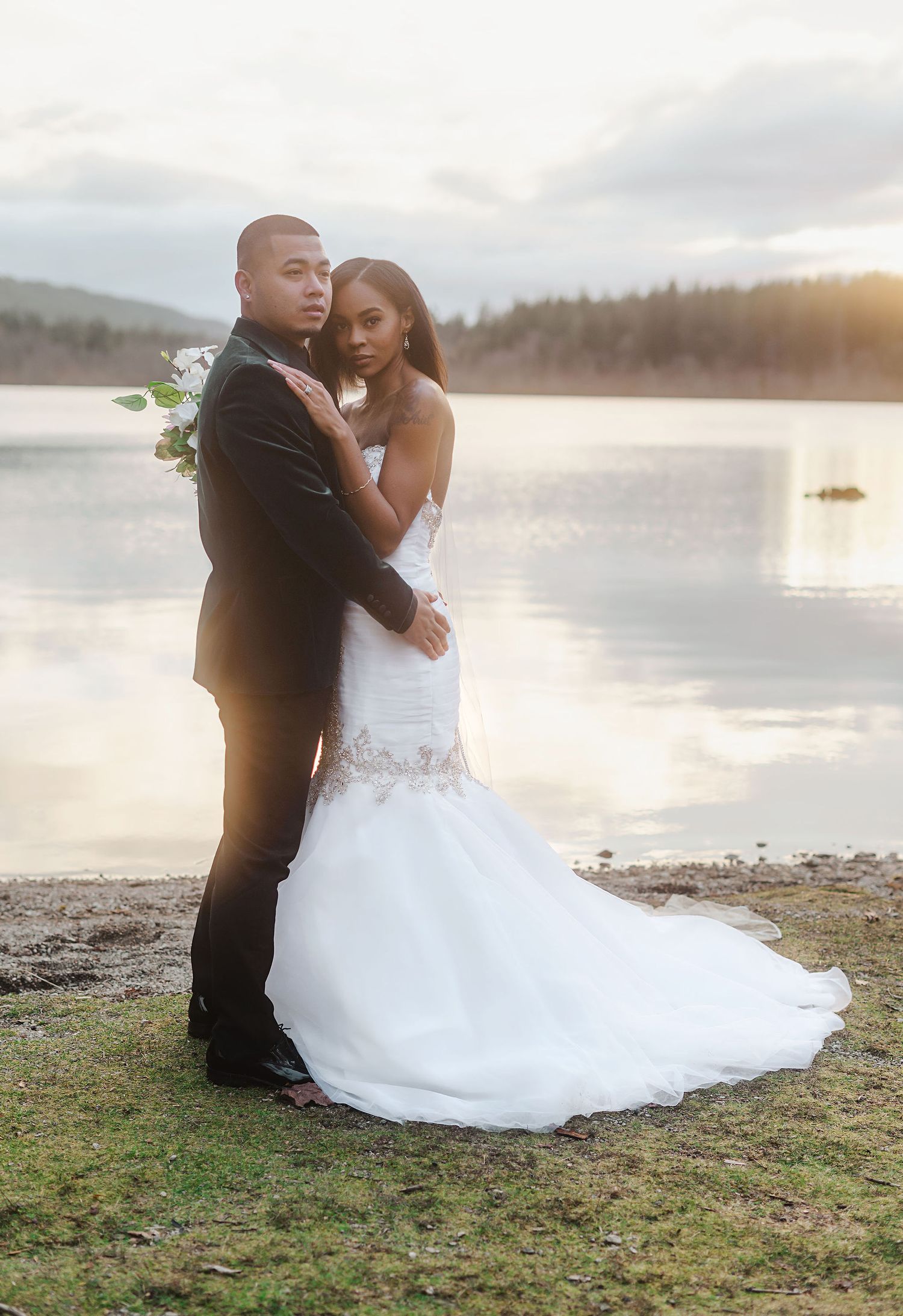 Romantic sunset wedding portraits captured by a lake with mountains in the background.