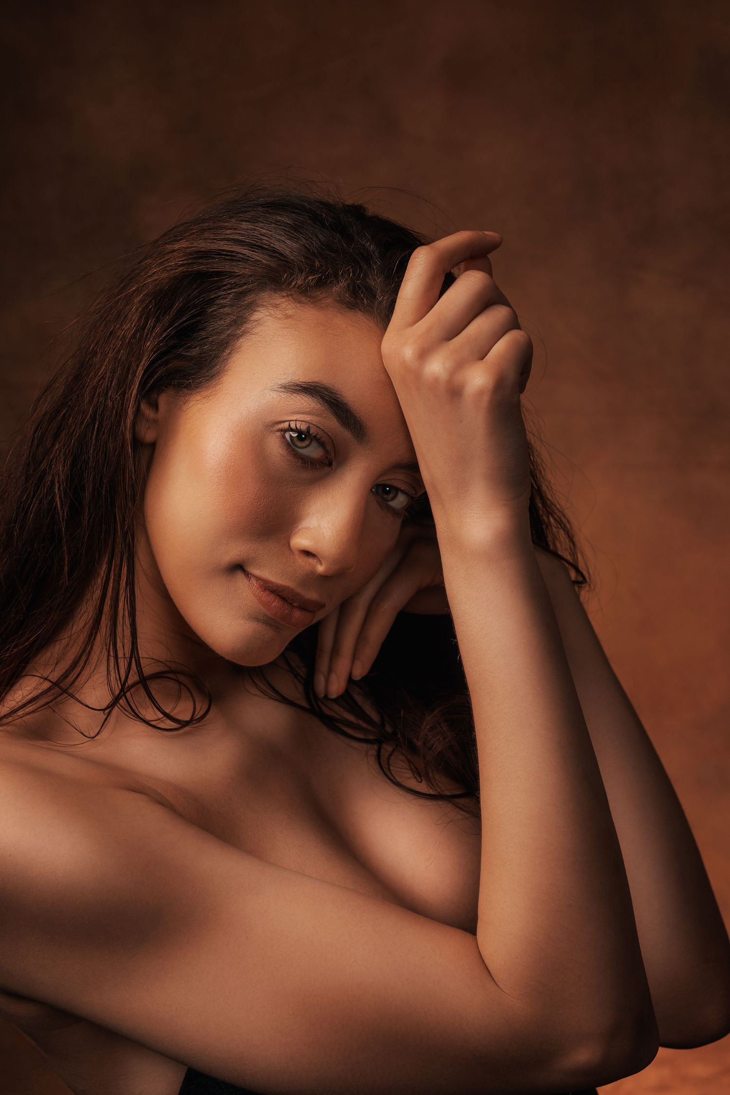 Artistic portrait photograph with warm lighting and shadows against brown background.