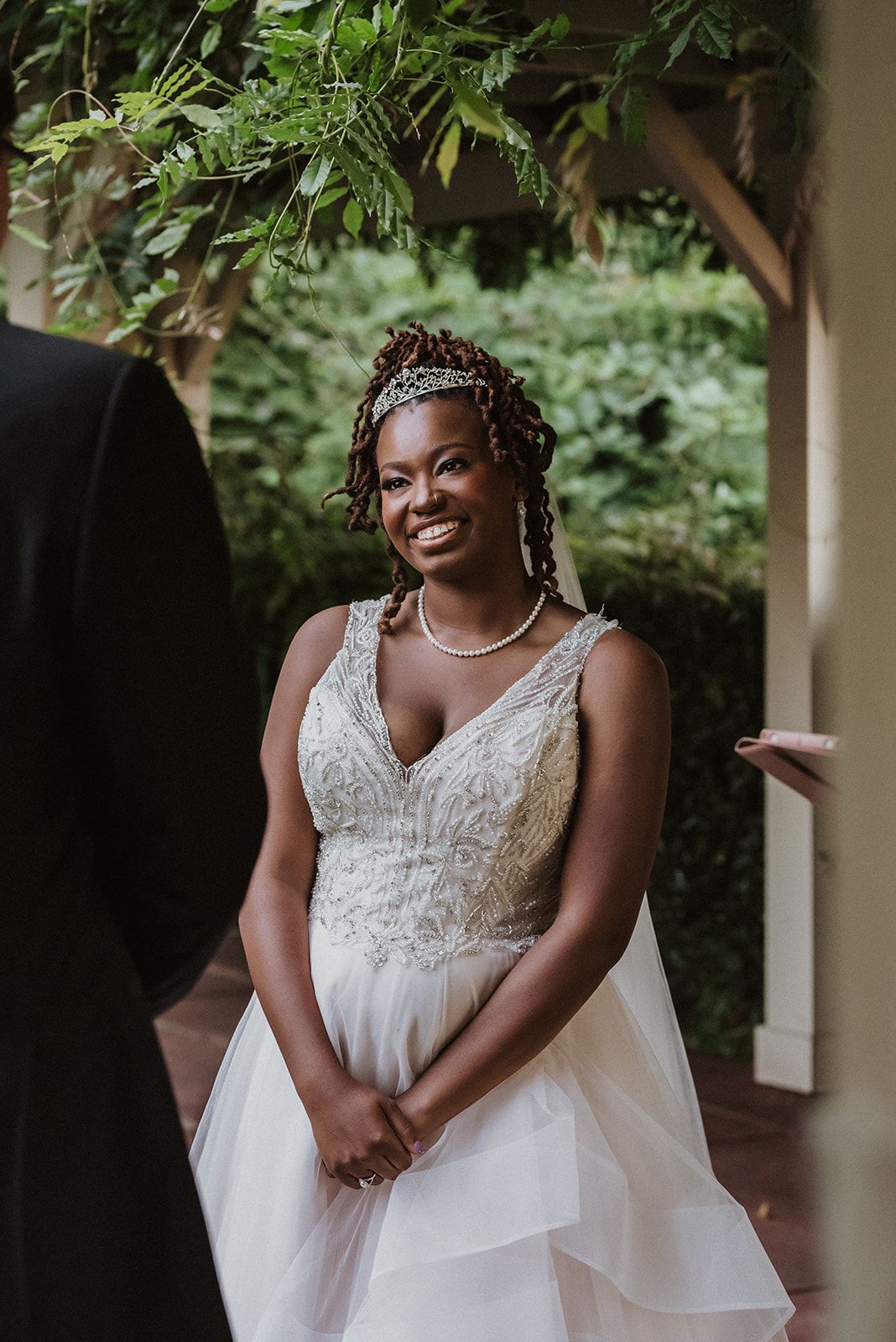 A radiant bride poses in a flowing white lace wedding gown with ruffled skirt details.