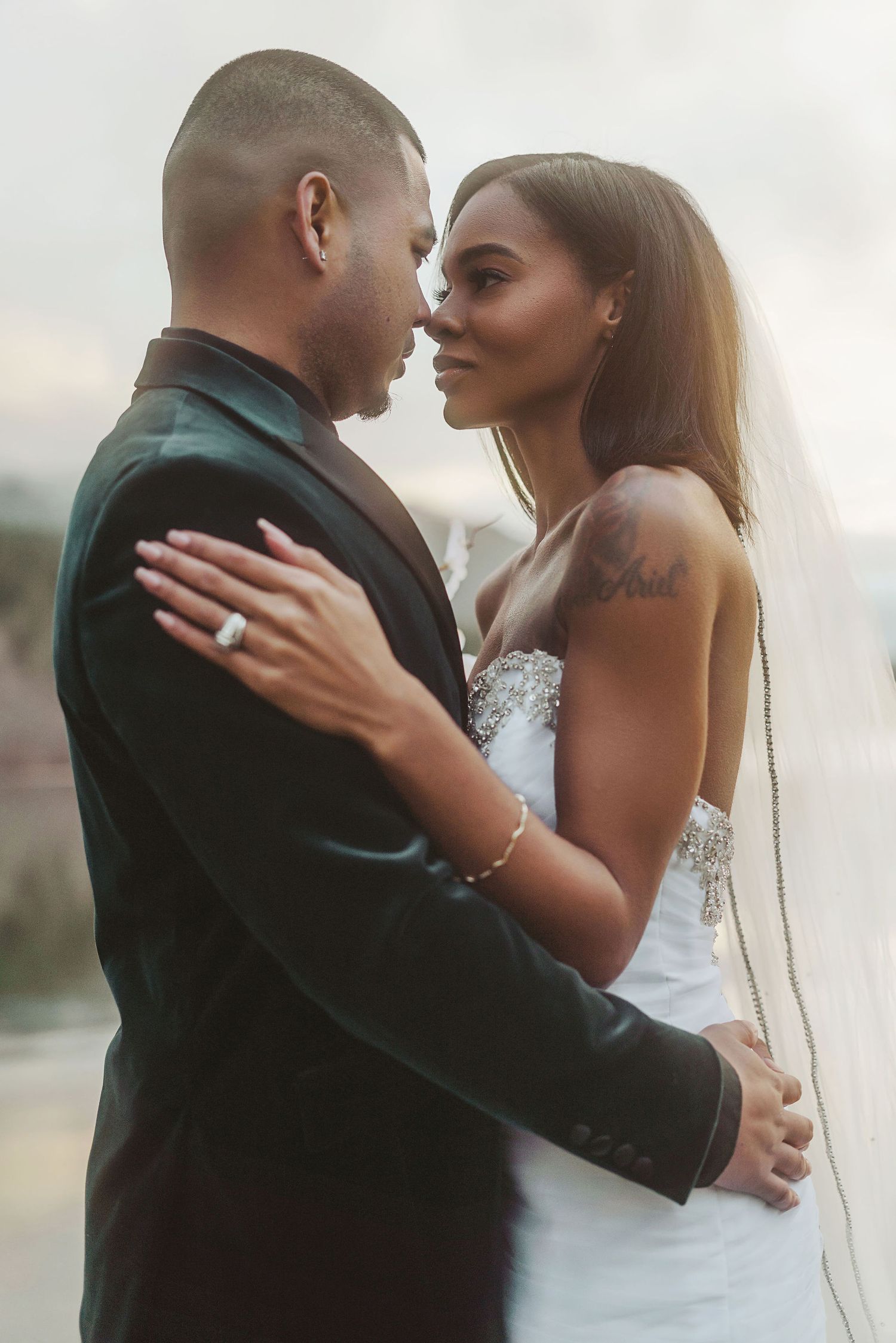 Tender wedding couple embraces during sunset photoshoot by the water.